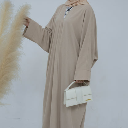 Person wearing a beige corduroy abaya with a white background and a vase with dried plants on the left. EverydayCorduroyAbaya_Beige1 - Noor & Grace