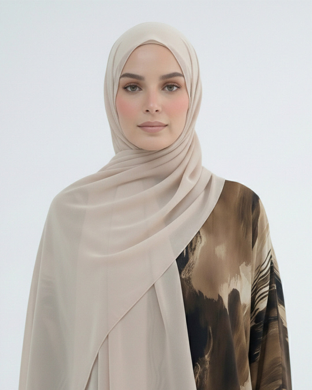 Woman wearing a beige hijab and a patterned top on a white background