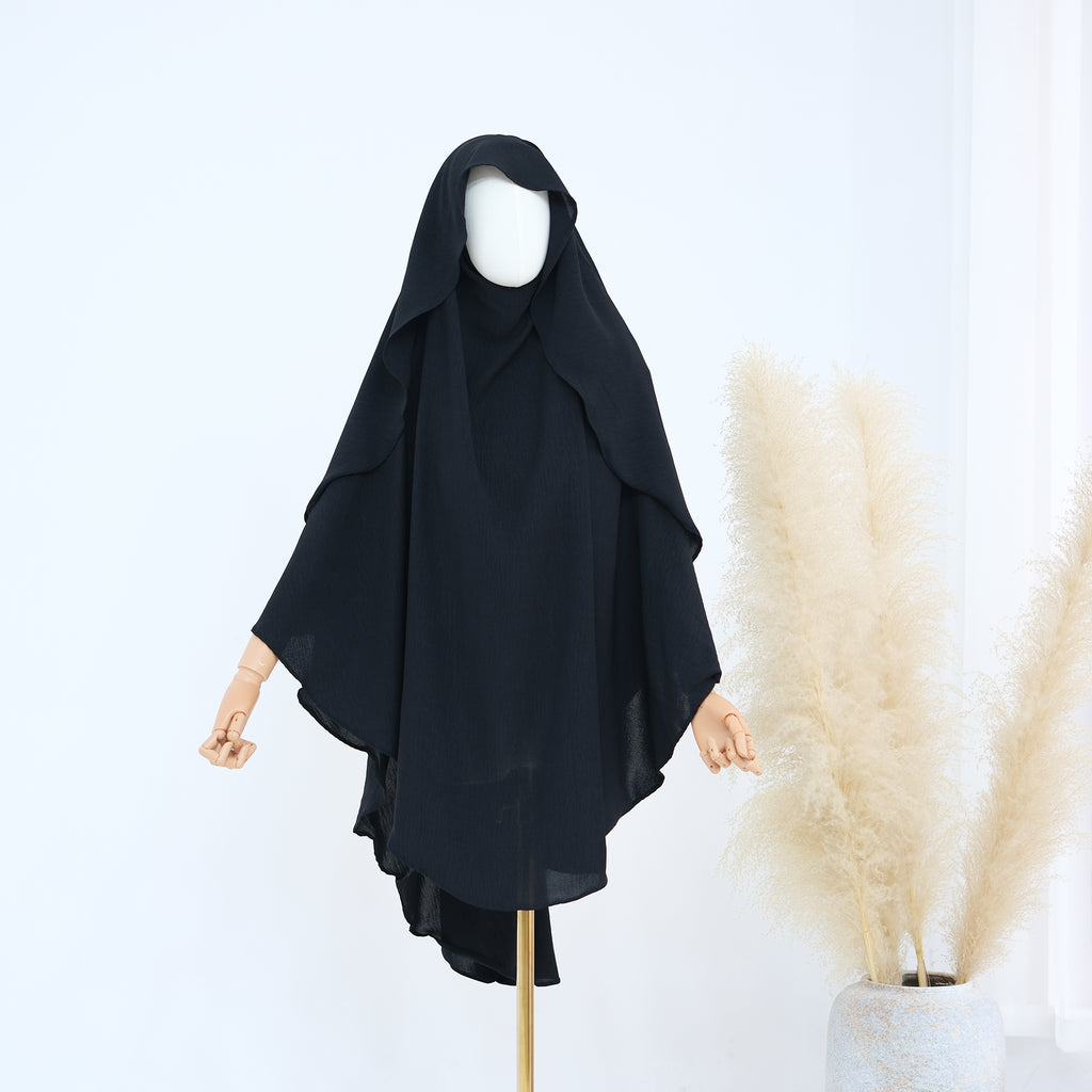 Black abaya on a mannequin against a white background with pampas grass.