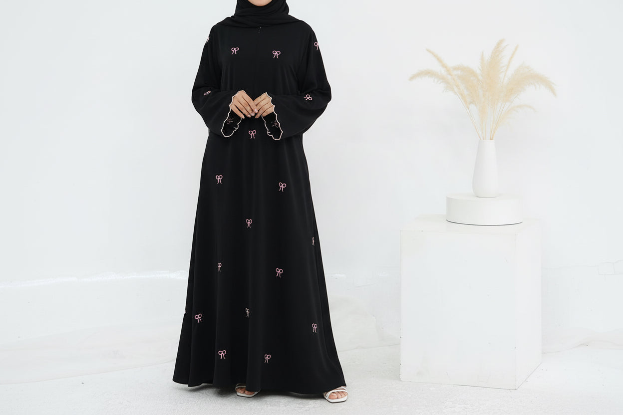 Woman wearing a black abaya with white patterns on a white background