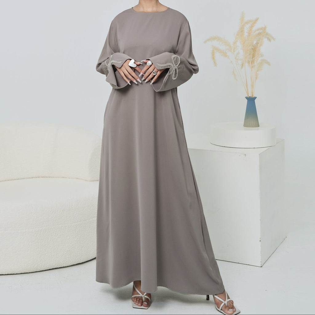 Woman wearing a long, light gray dress standing in a minimalistic room with a white couch and vase.