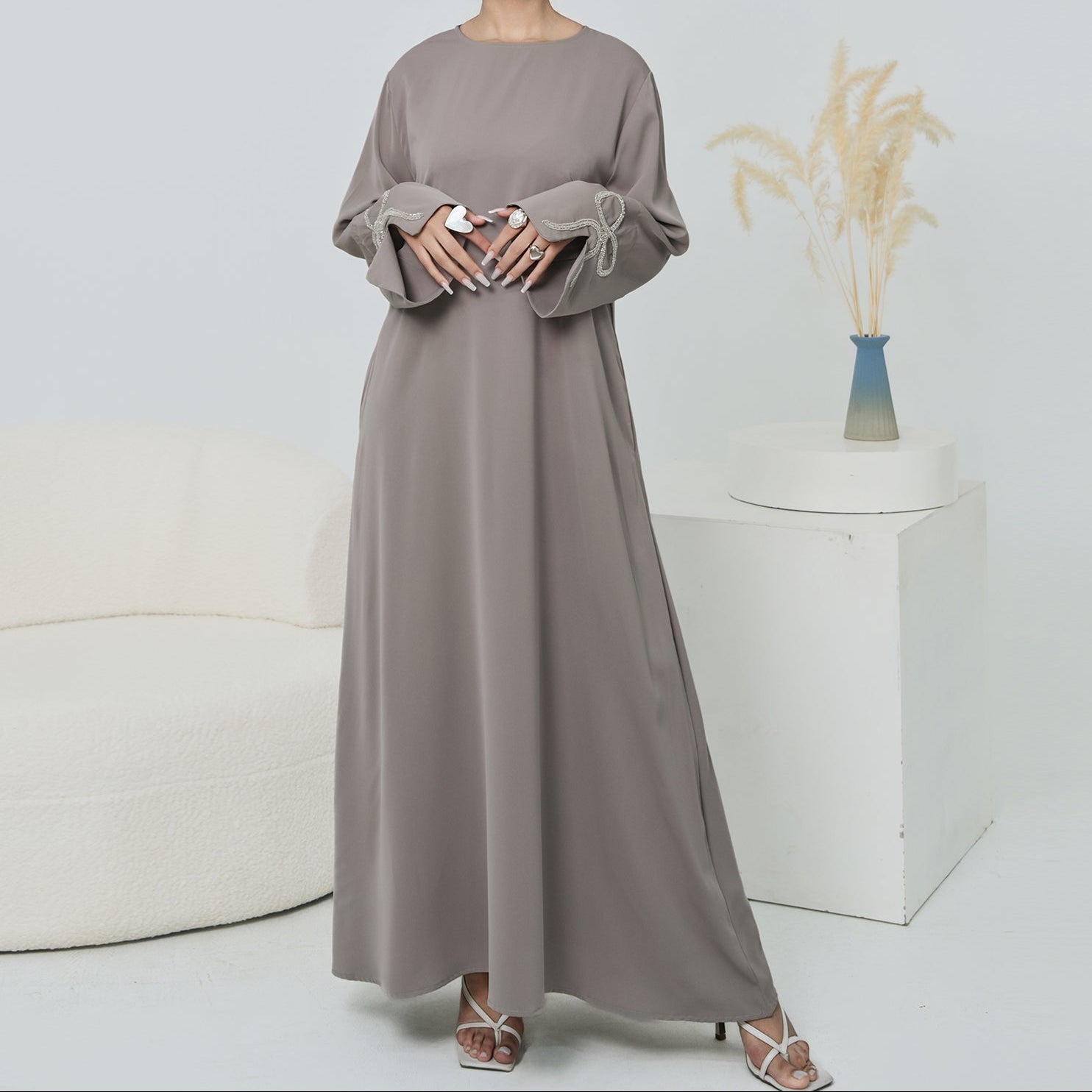 Woman wearing a long, light gray dress standing in a minimalistic room with a white couch and vase.