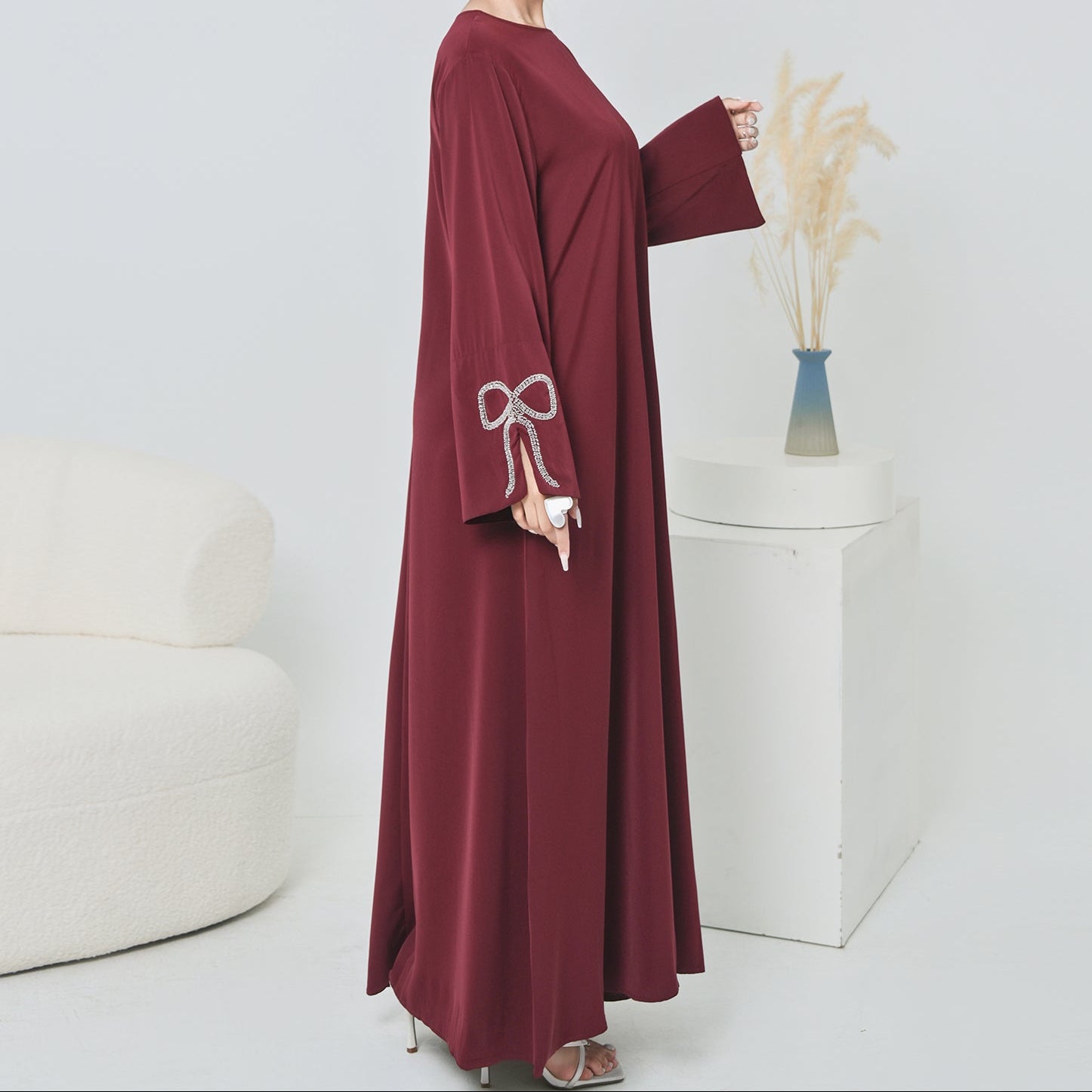 Woman wearing a burgundy abaya with a bow detail in a minimalistic setting.