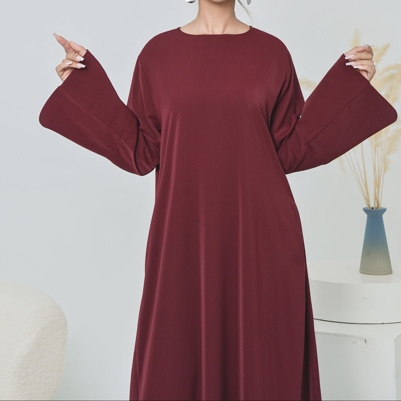 Woman wearing a burgundy dress with wide sleeves against a plain background