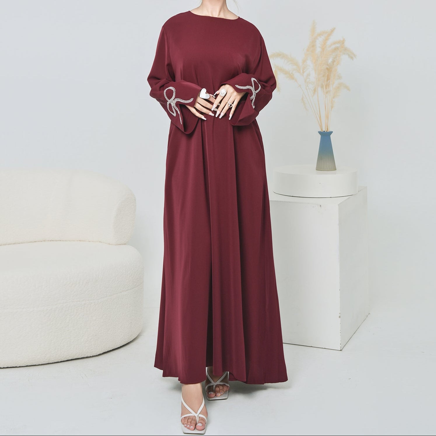 Woman wearing a burgundy dress with white embroidery in a minimalistic setting.