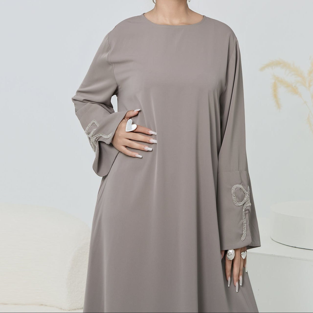 Woman wearing a long, light brown dress with floral embroidery on a plain background