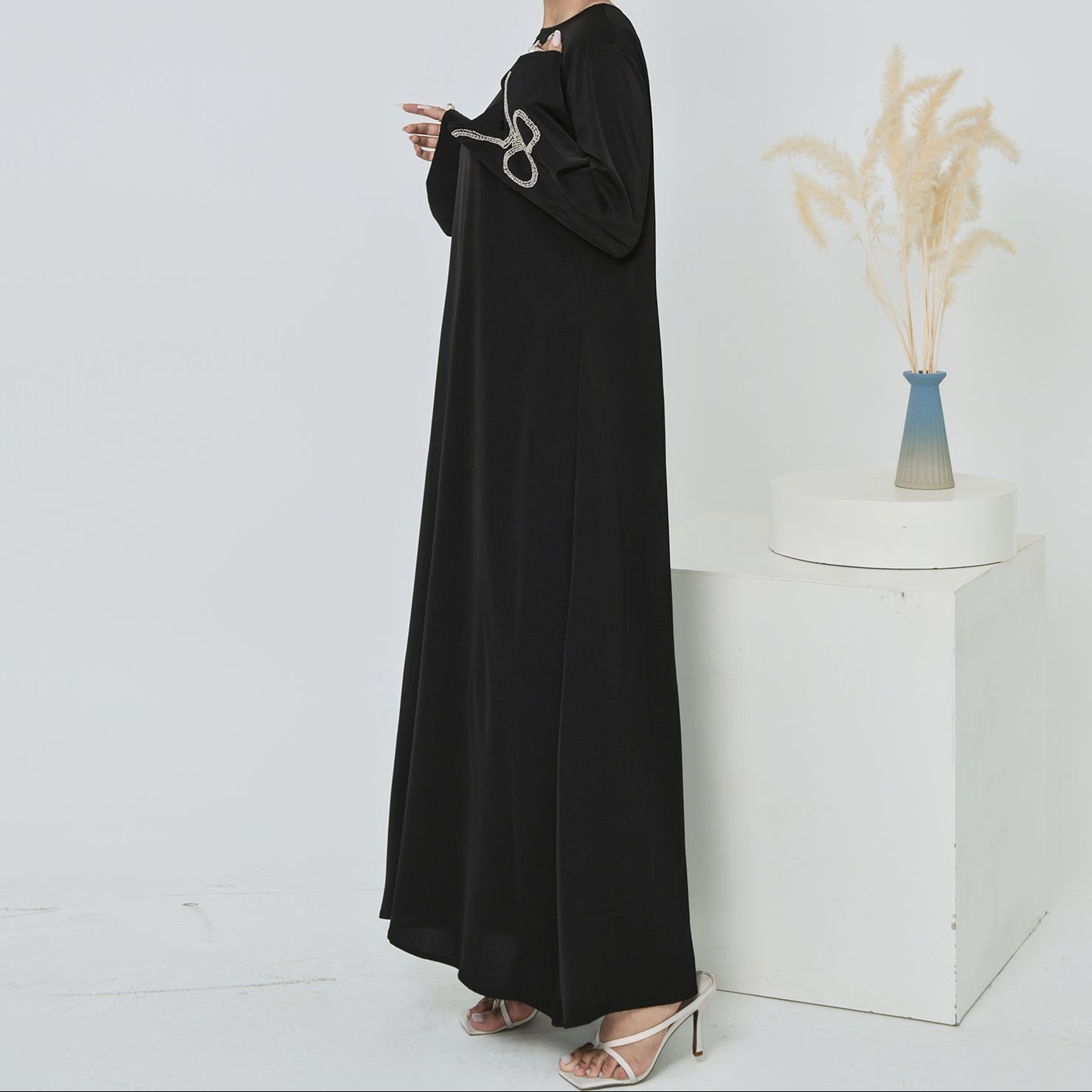 Woman wearing a black abaya standing against a white background
