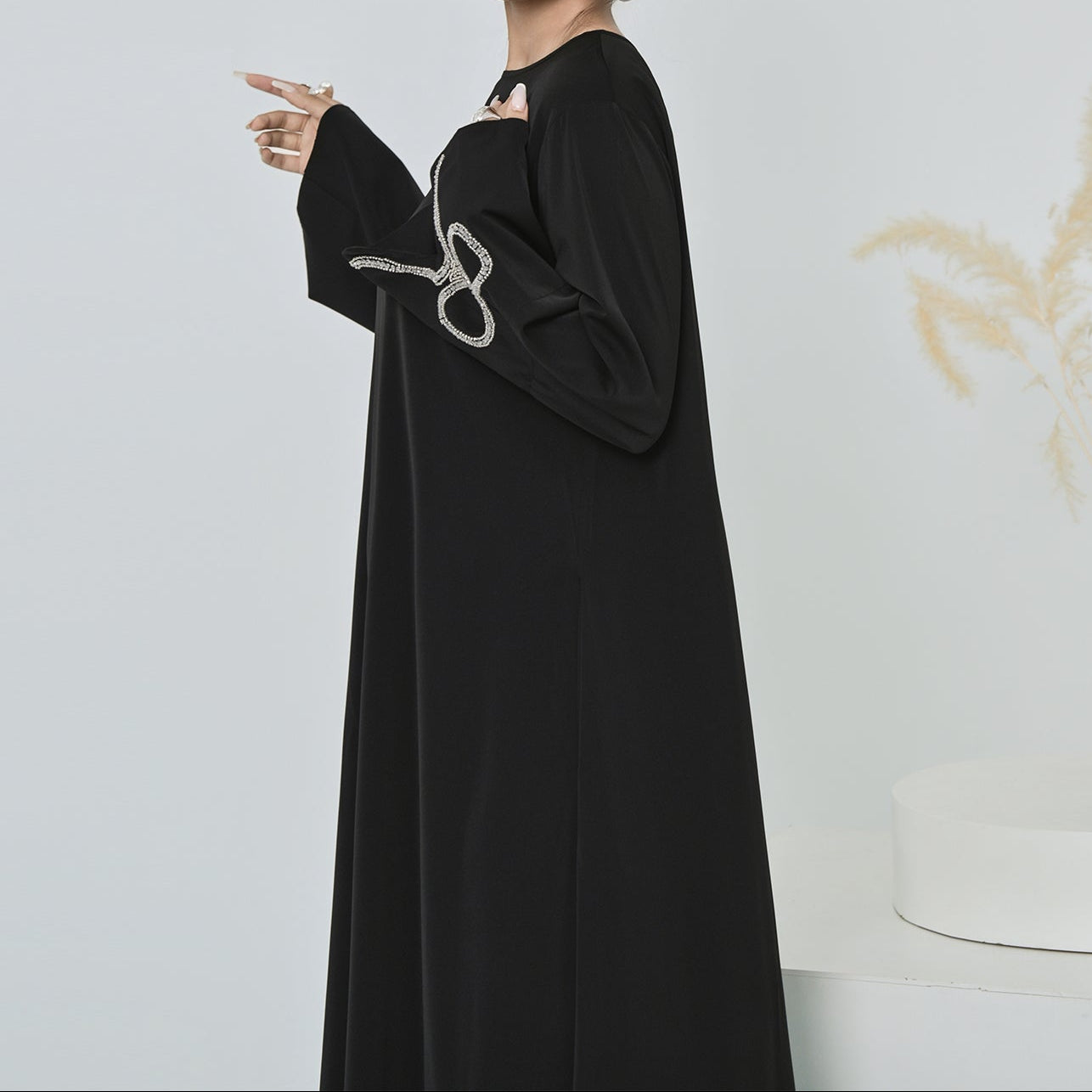 Woman in a black dress standing next to a vase with dried plants on a white background