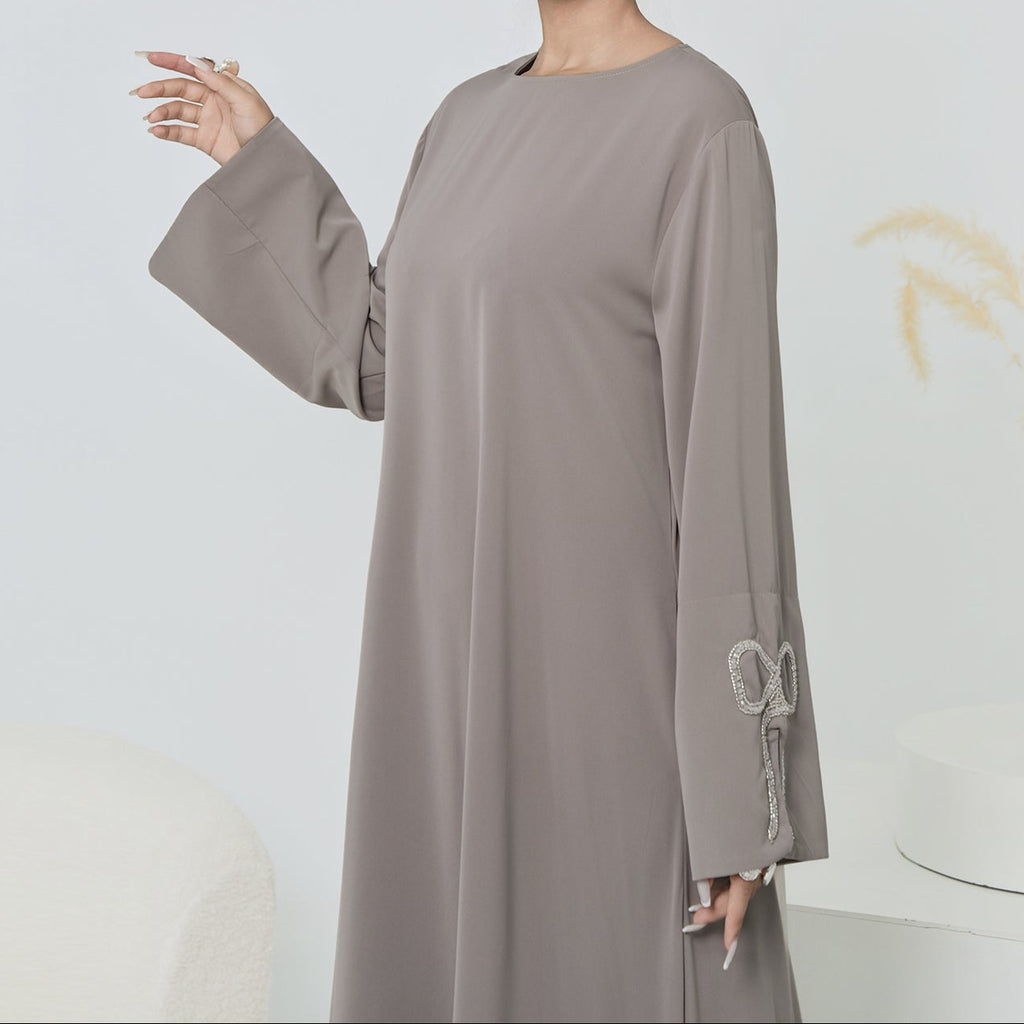 Woman wearing a long, light gray dress with a white background