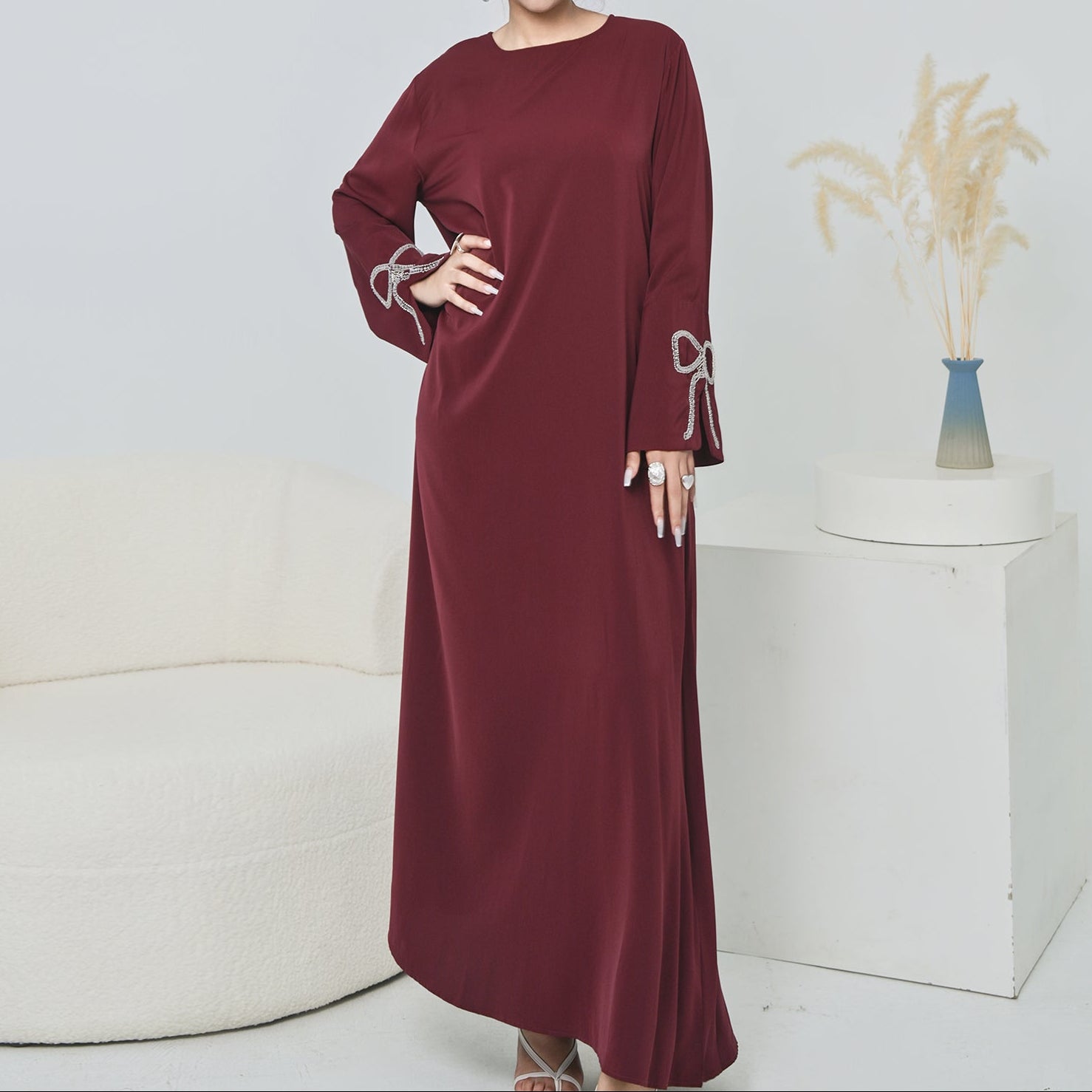 Woman wearing a burgundy dress with decorative sleeves in a minimalistic setting.