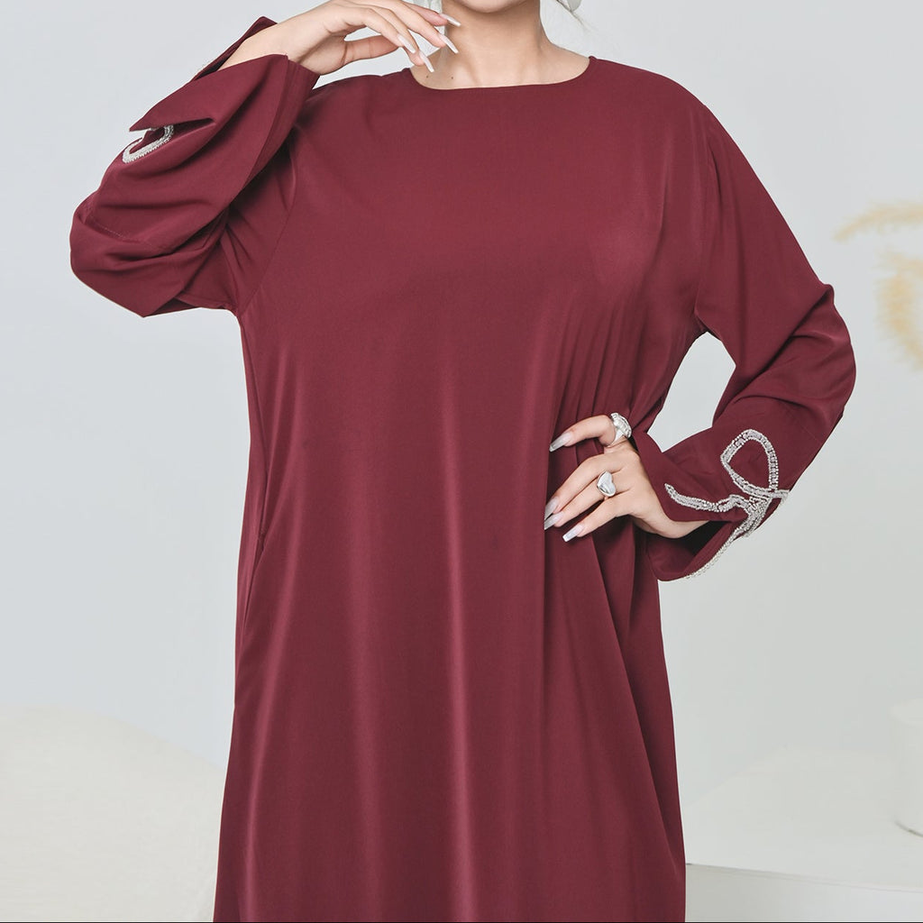 Woman wearing a burgundy dress with long sleeves on a light gray background