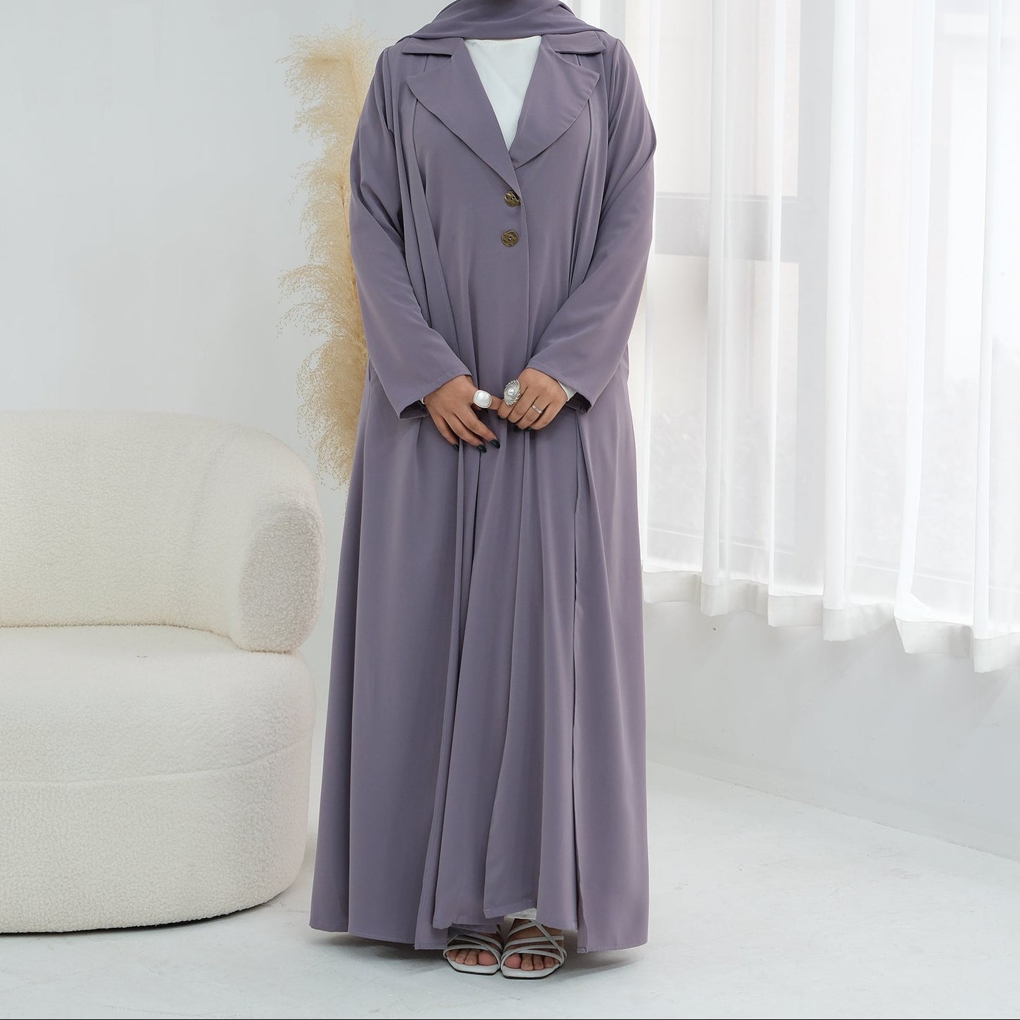 Woman wearing a long, light purple dress with buttons in a minimalistic room.
