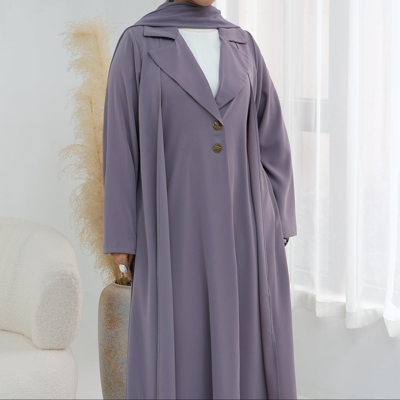 Woman wearing a long, light purple dress with a white top in a bright room.