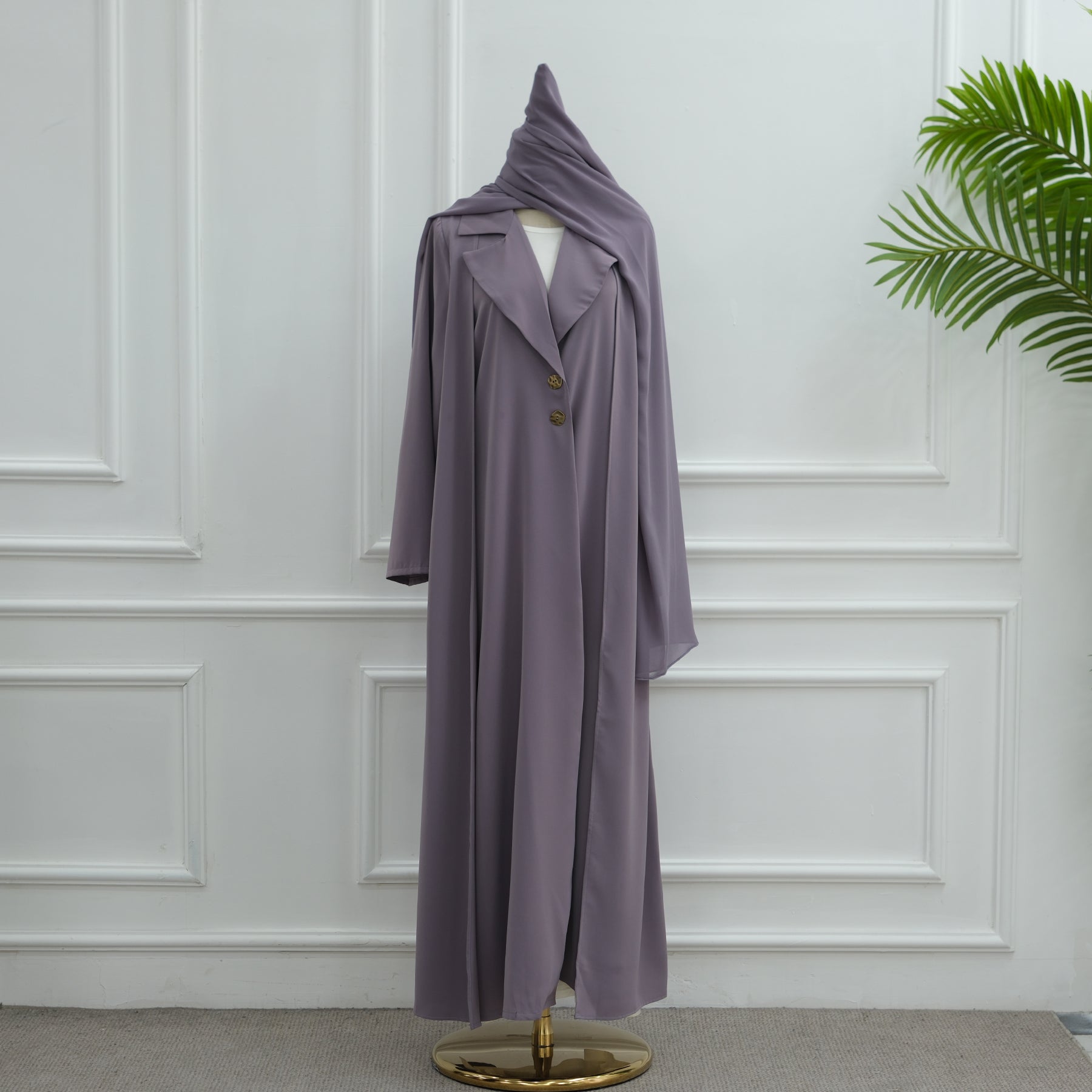 Purple coat on a mannequin against a white paneled wall with a plant to the side.