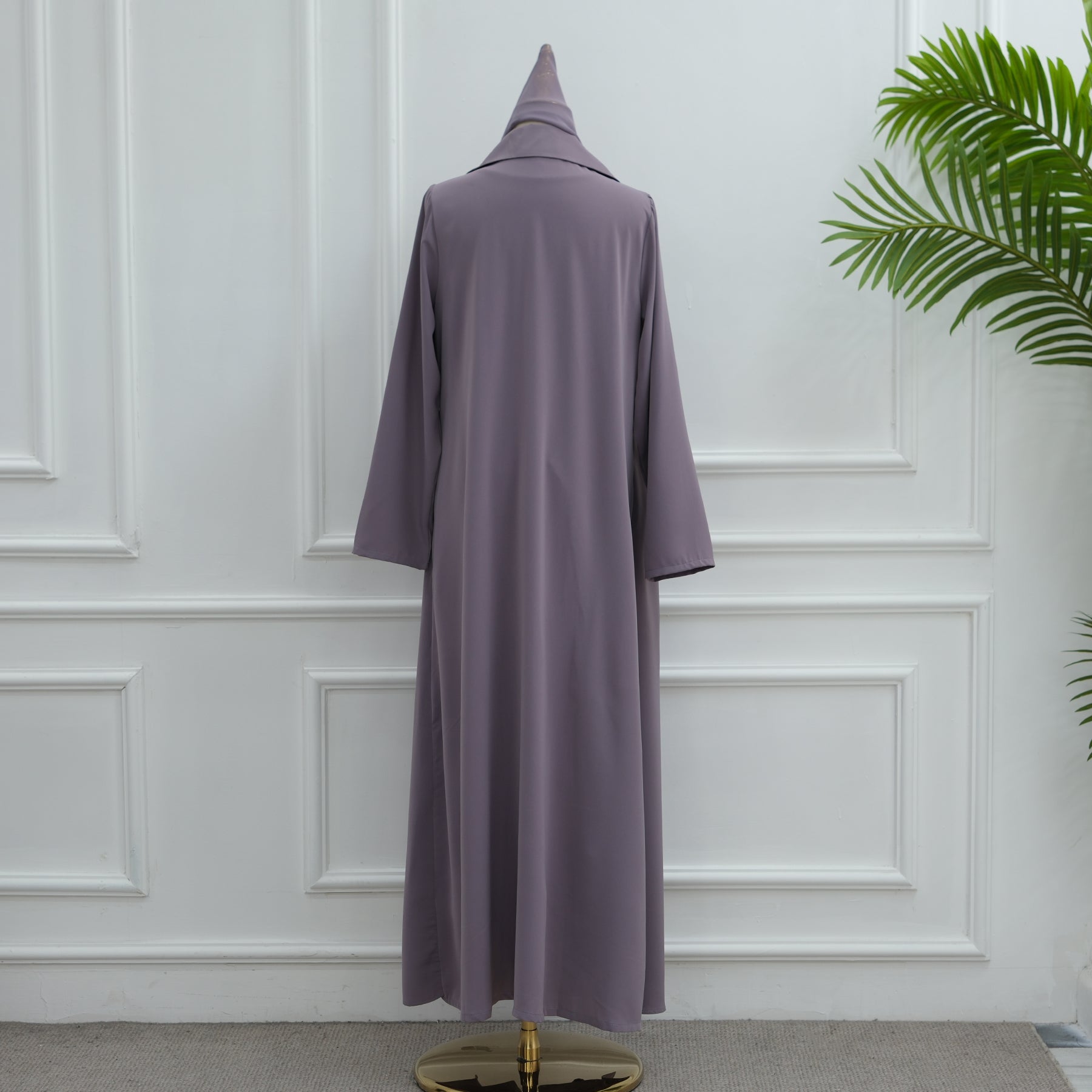 Purple dress on a mannequin against a white paneled wall with a plant in the corner.