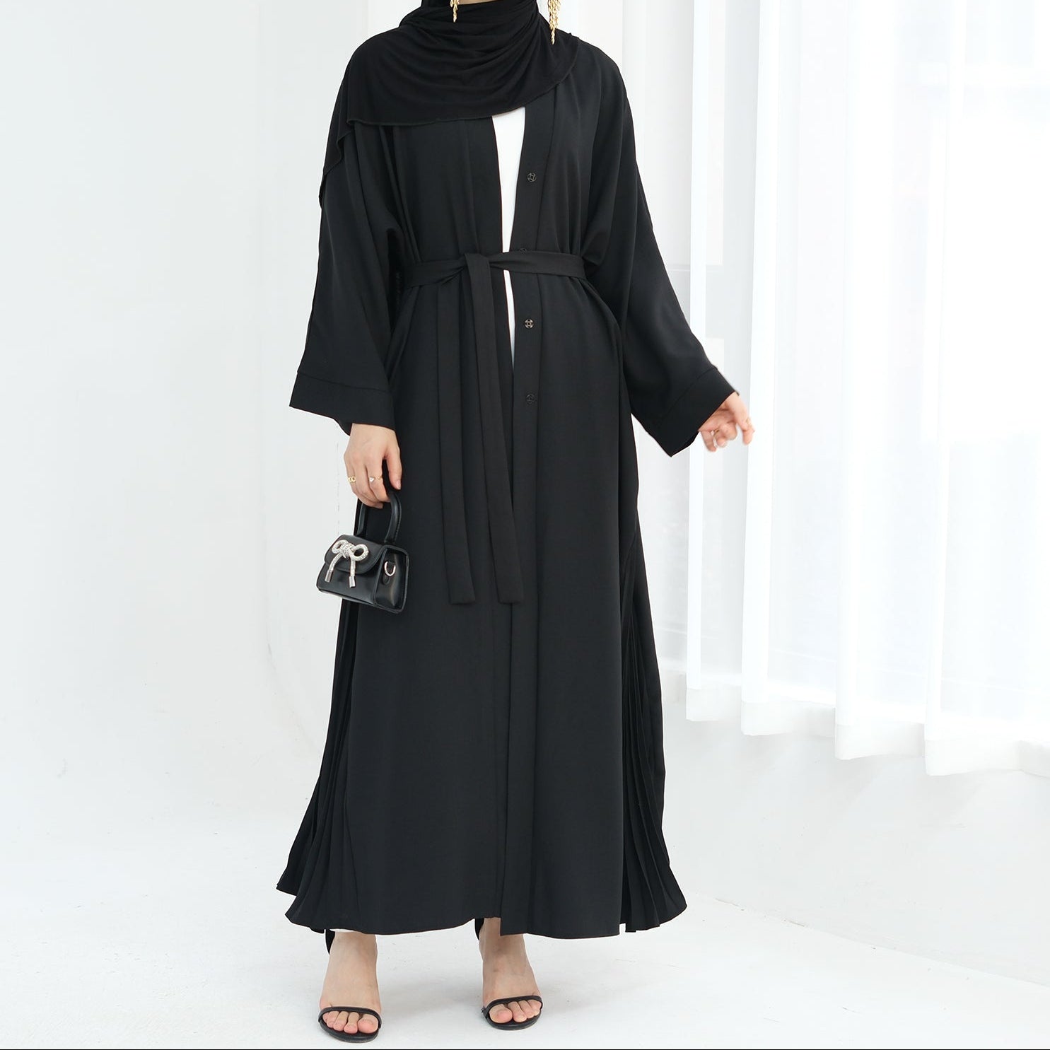 Woman wearing a black abaya against a white background. Abaya Al-Tayyat Al-Aneeqa (عباءة الطيات الأنيقة) - Noor & Grace