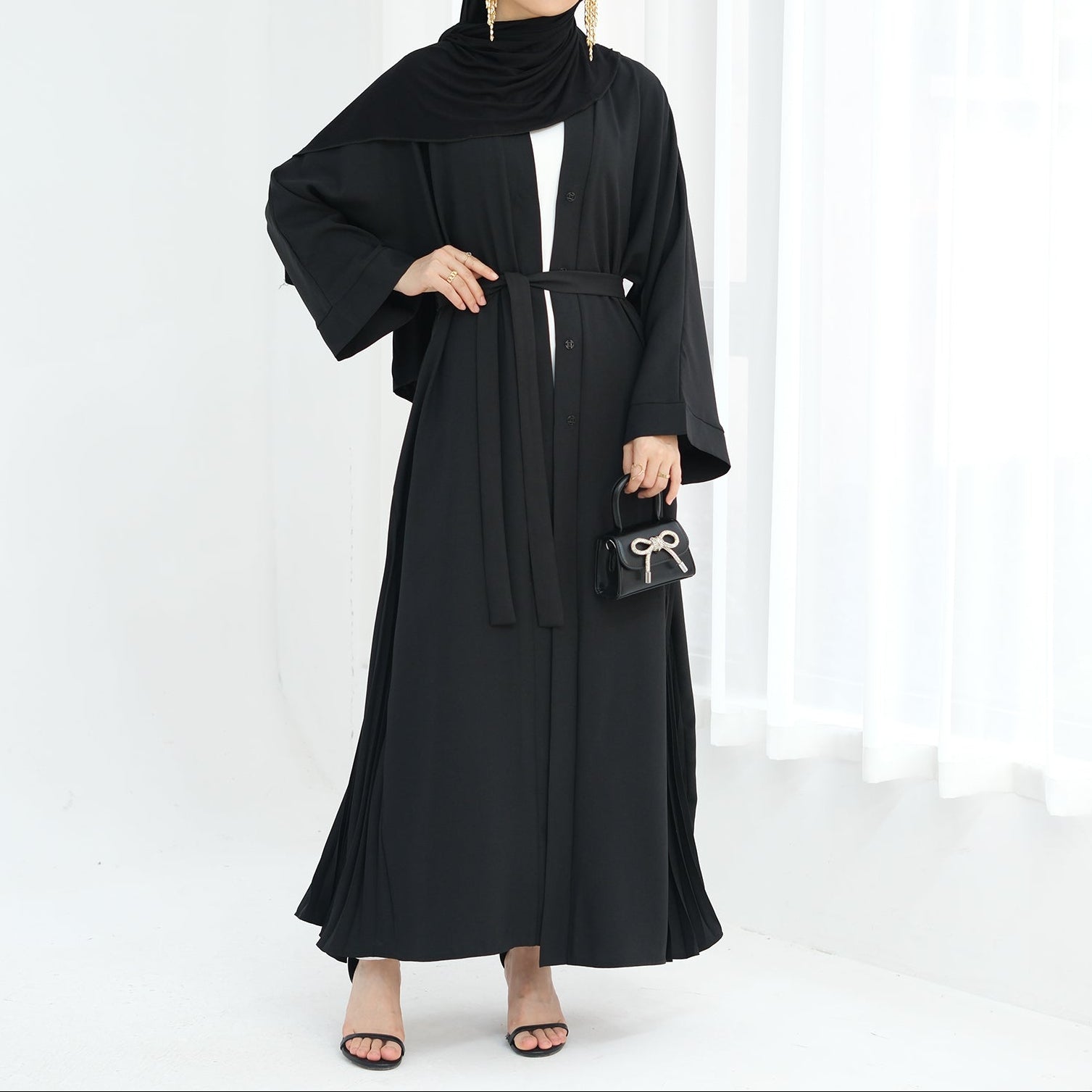 Woman wearing a black abaya against a white background. Abaya Al-Tayyat Al-Aneeqa (عباءة الطيات الأنيقة) - Noor & Grace