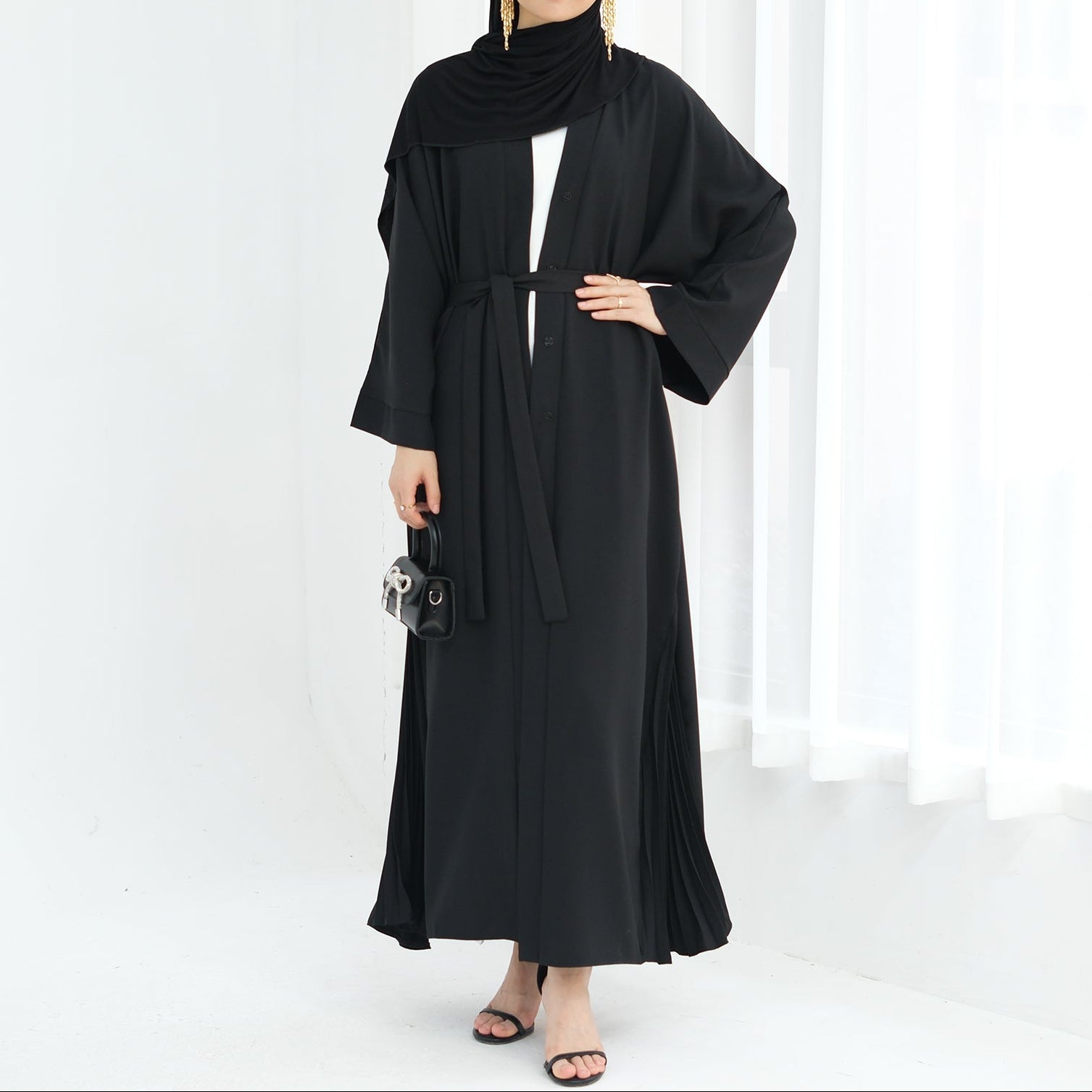 Woman wearing a black abaya against a white background. Abaya Al-Tayyat Al-Aneeqa (عباءة الطيات الأنيقة) - Noor & Grace