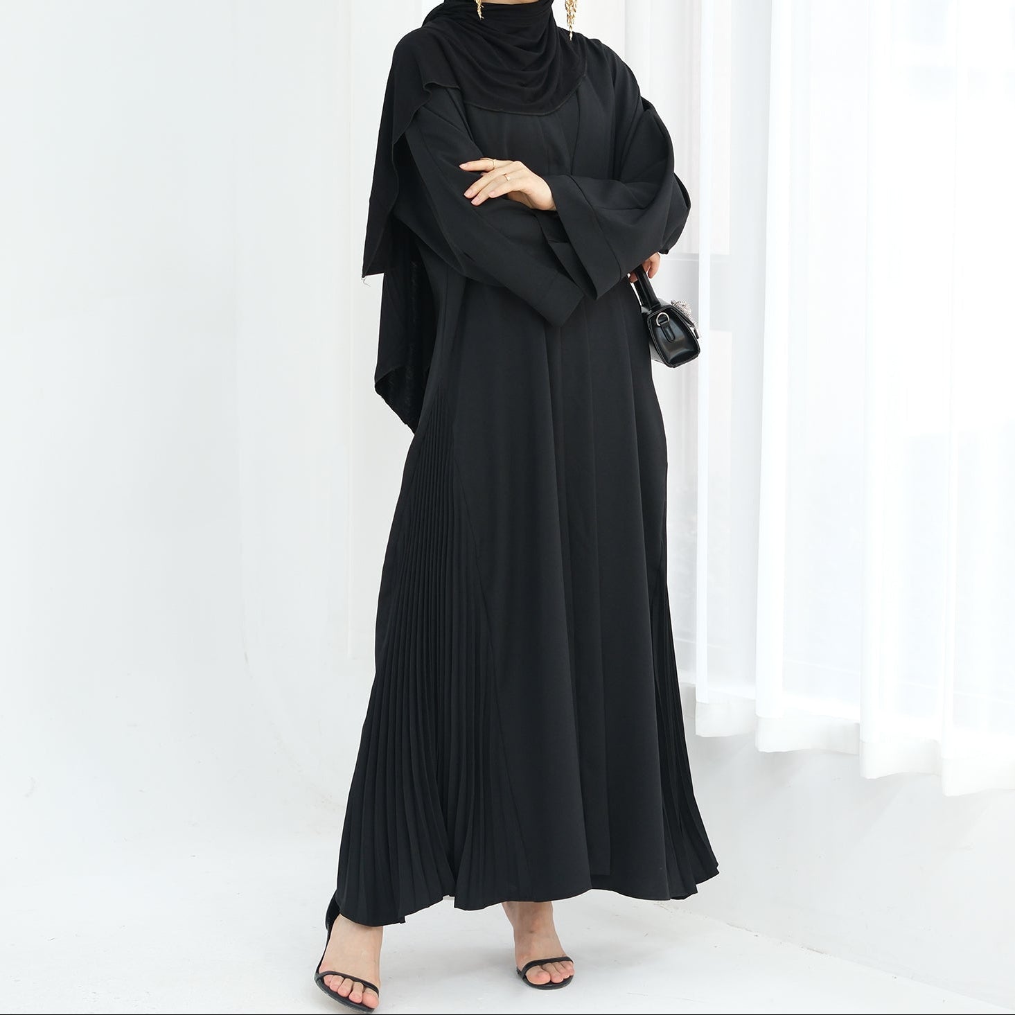 Woman wearing a black abaya against a white background. Abaya Al-Tayyat Al-Aneeqa (عباءة الطيات الأنيقة) - Noor & Grace