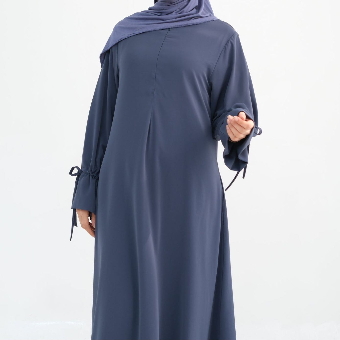 Woman wearing a long blue dress with a matching hijab on a white background
