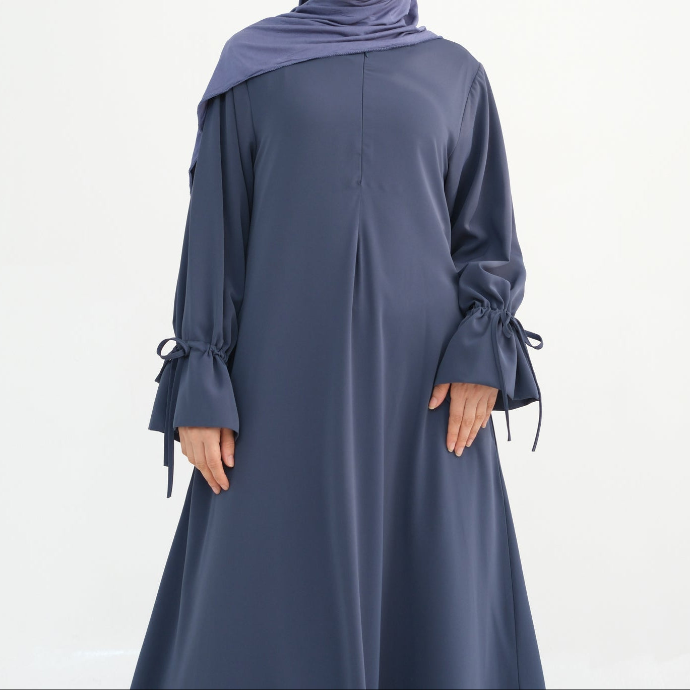 Woman wearing a long-sleeve gray dress with a matching hijab on a white background