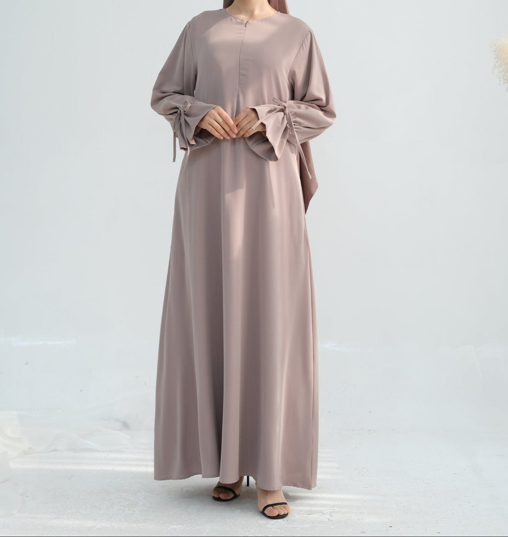 Woman wearing a long, light brown dress with a matching headscarf on a white background