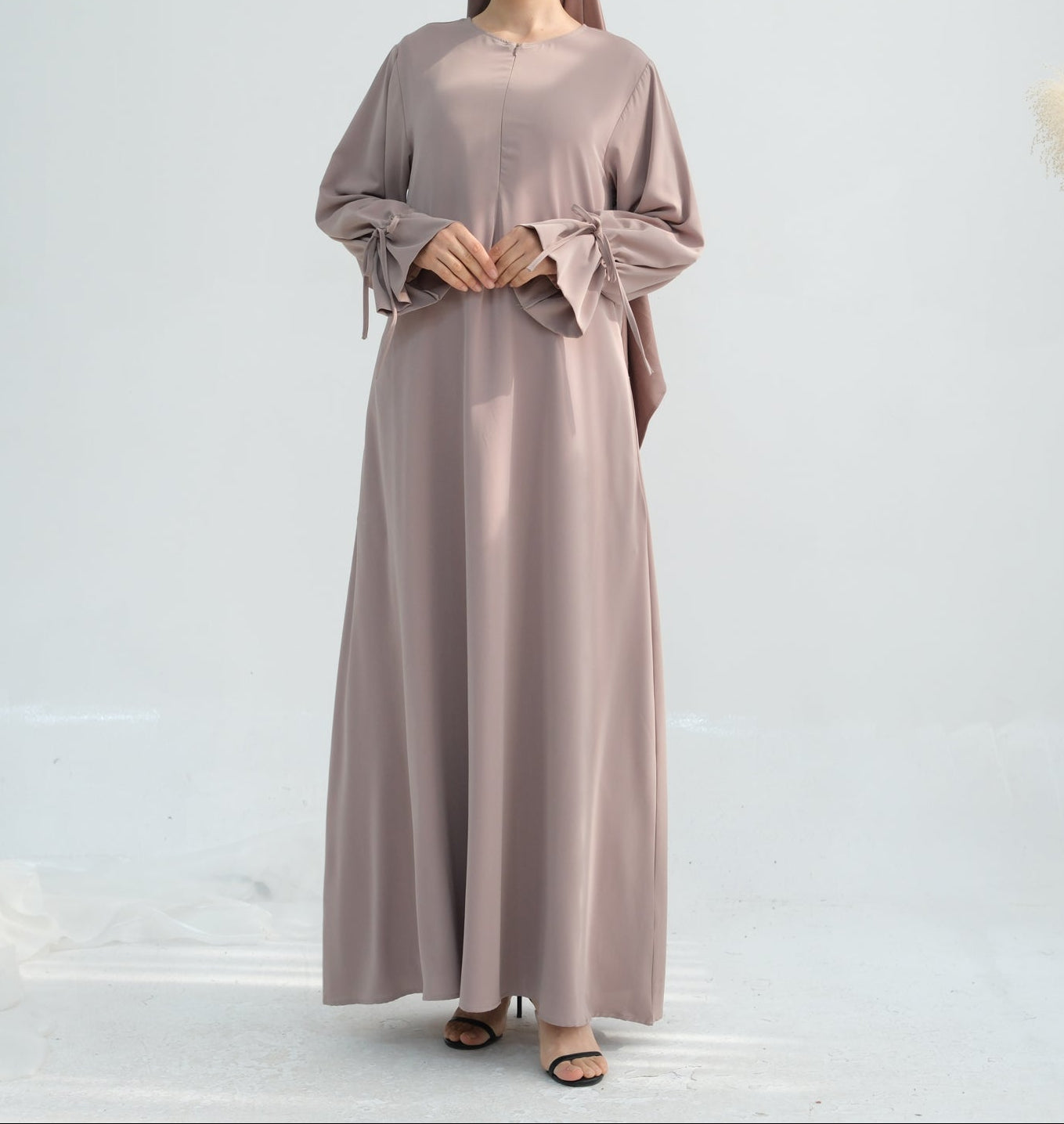 Woman wearing a long, light brown dress with a matching headscarf on a white background