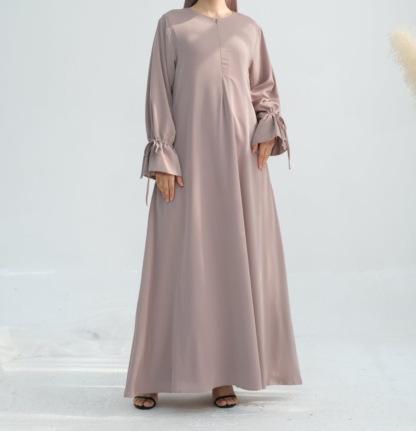 Woman wearing a long, light brown dress with a matching hijab on a white background