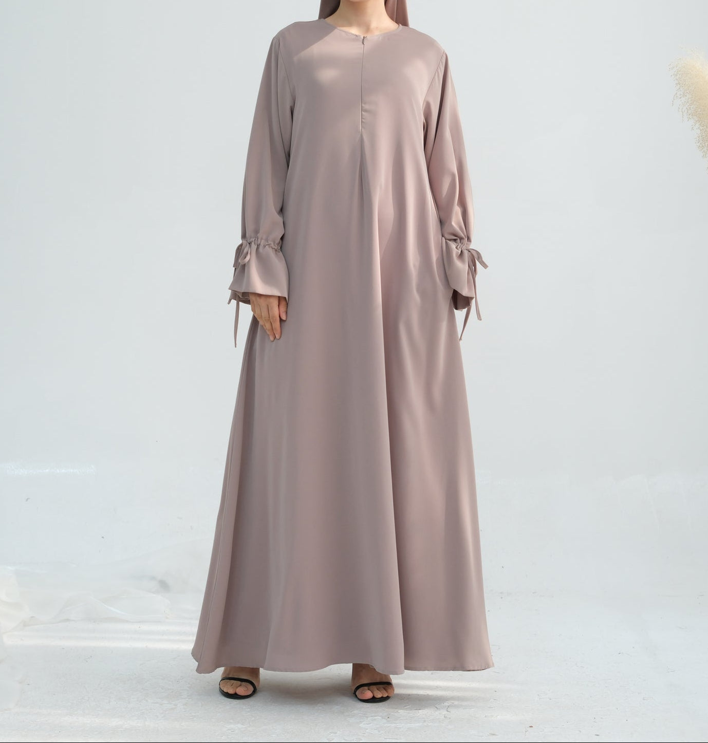 Woman wearing a long, light brown dress with a plain background