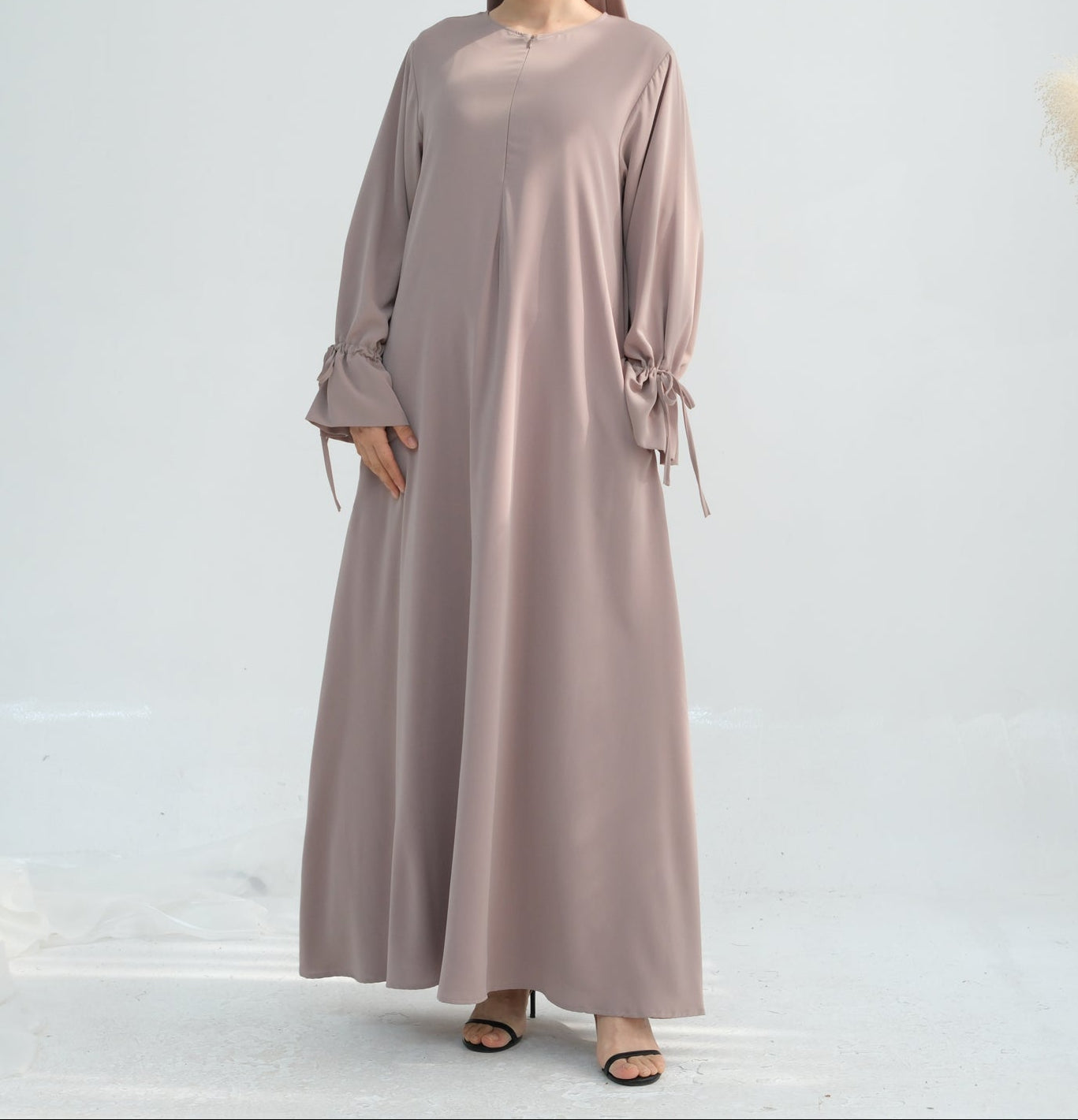 Woman wearing a long beige dress with a plain background