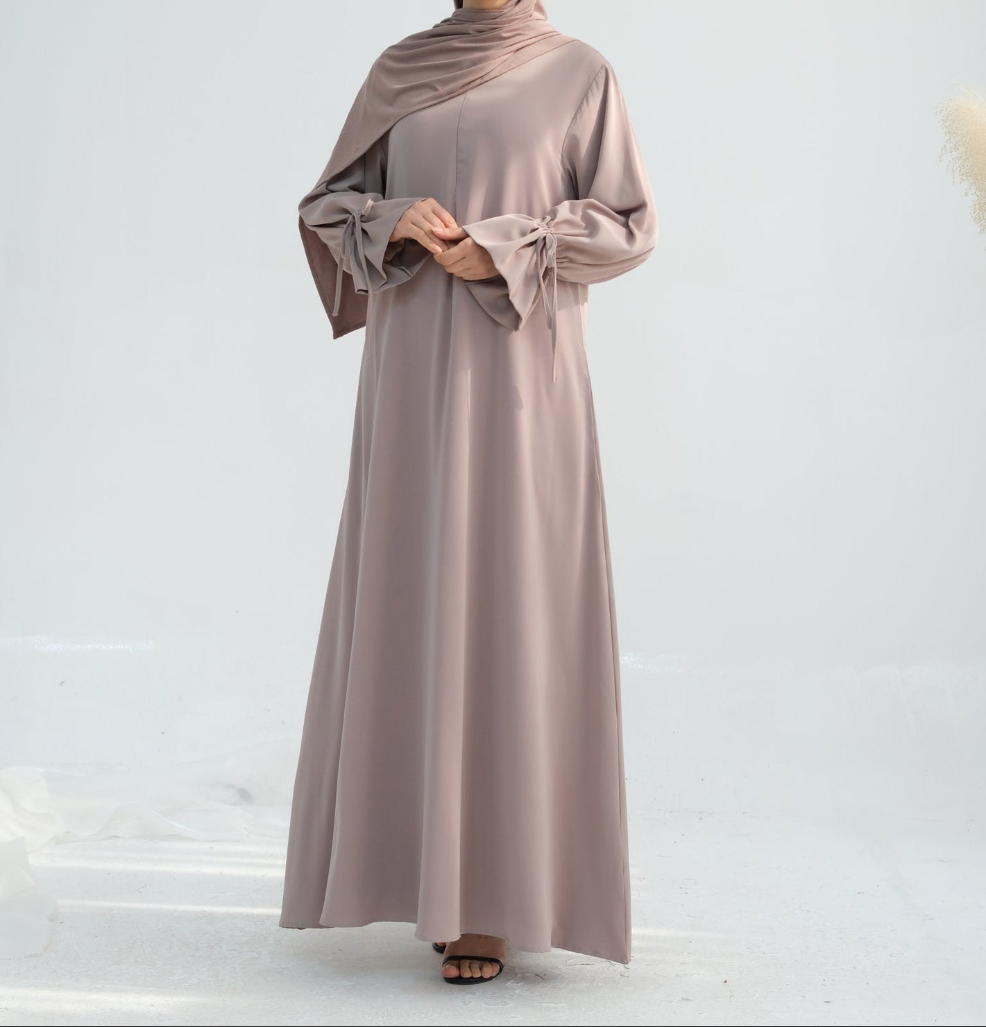 Woman wearing a long, light brown dress with a matching hijab on a white background