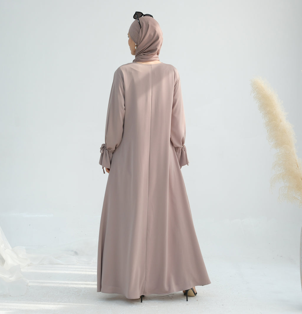 Woman wearing a long beige dress and matching hijab on a white background