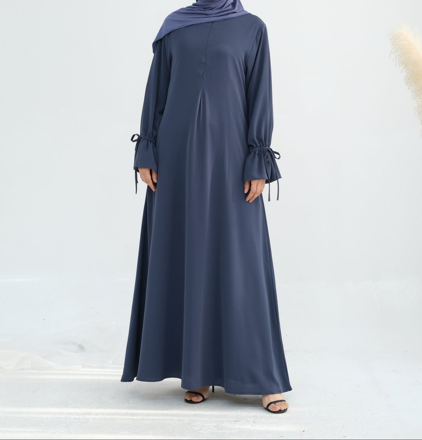Woman wearing a long navy blue dress with a matching hijab on a white background