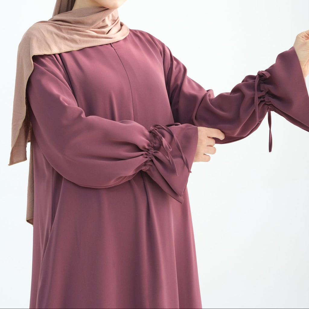Woman wearing a burgundy dress and beige hijab on a white background
