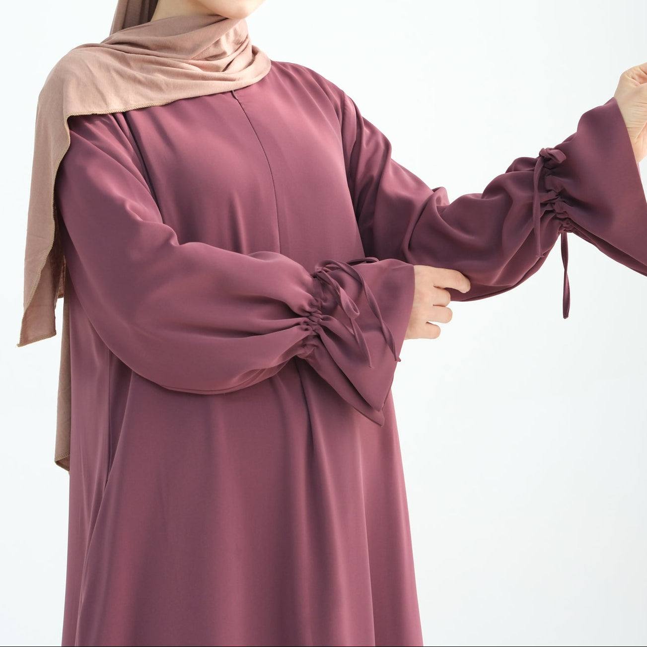 Woman wearing a burgundy dress and beige hijab on a white background