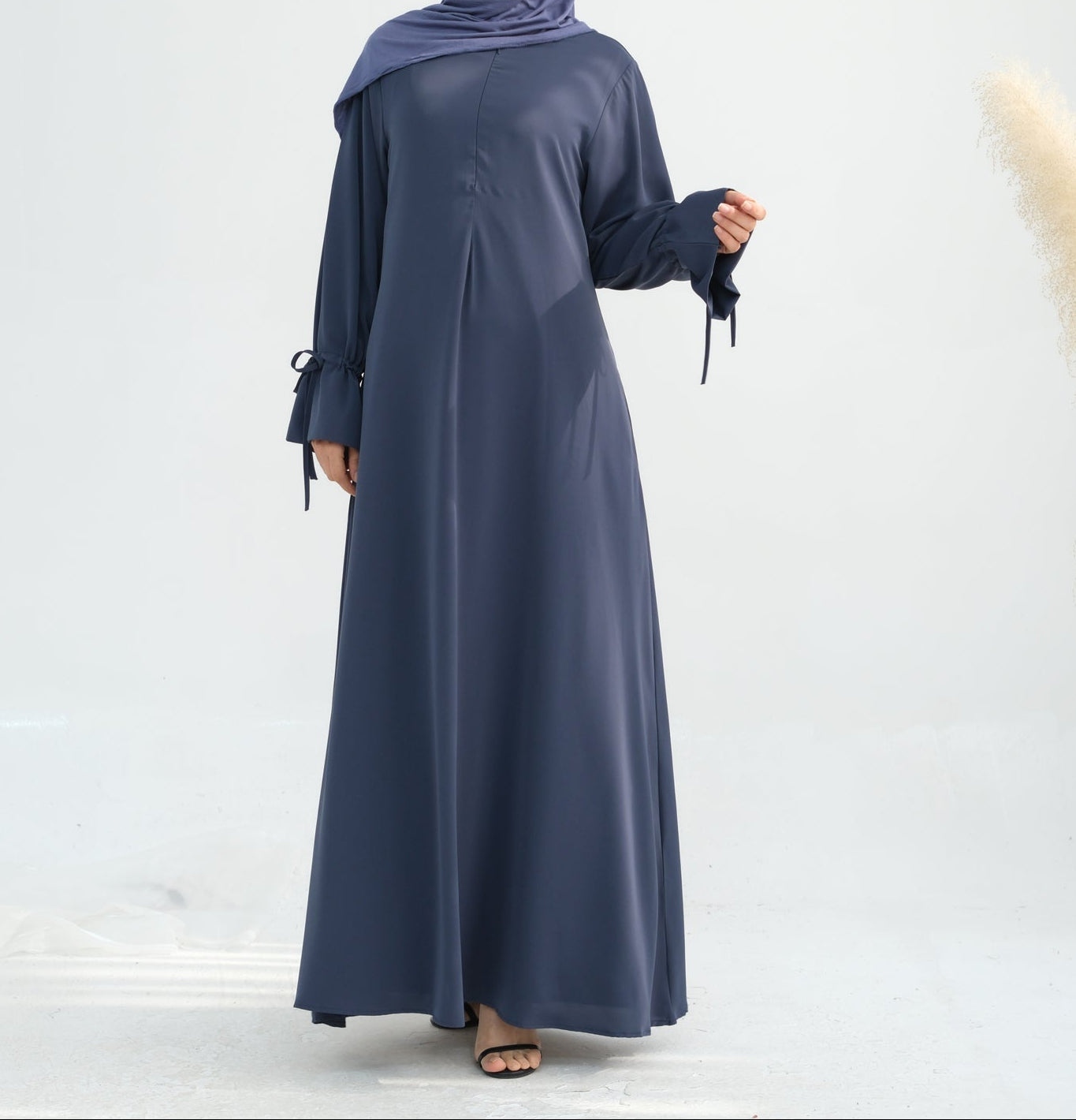 Woman wearing a long dark blue dress and hijab on a white background