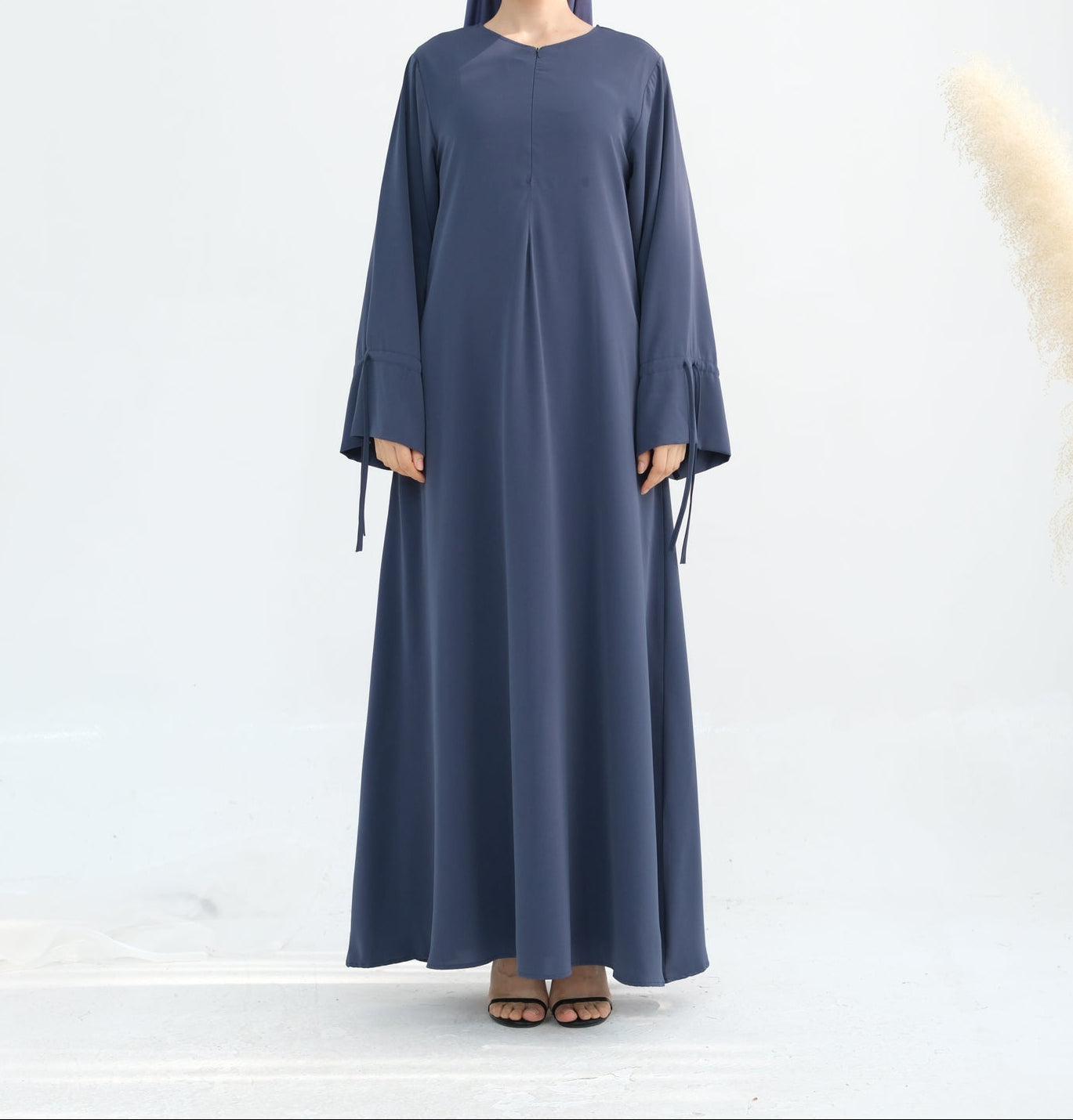 Woman wearing a long blue dress with a matching headscarf on a white background