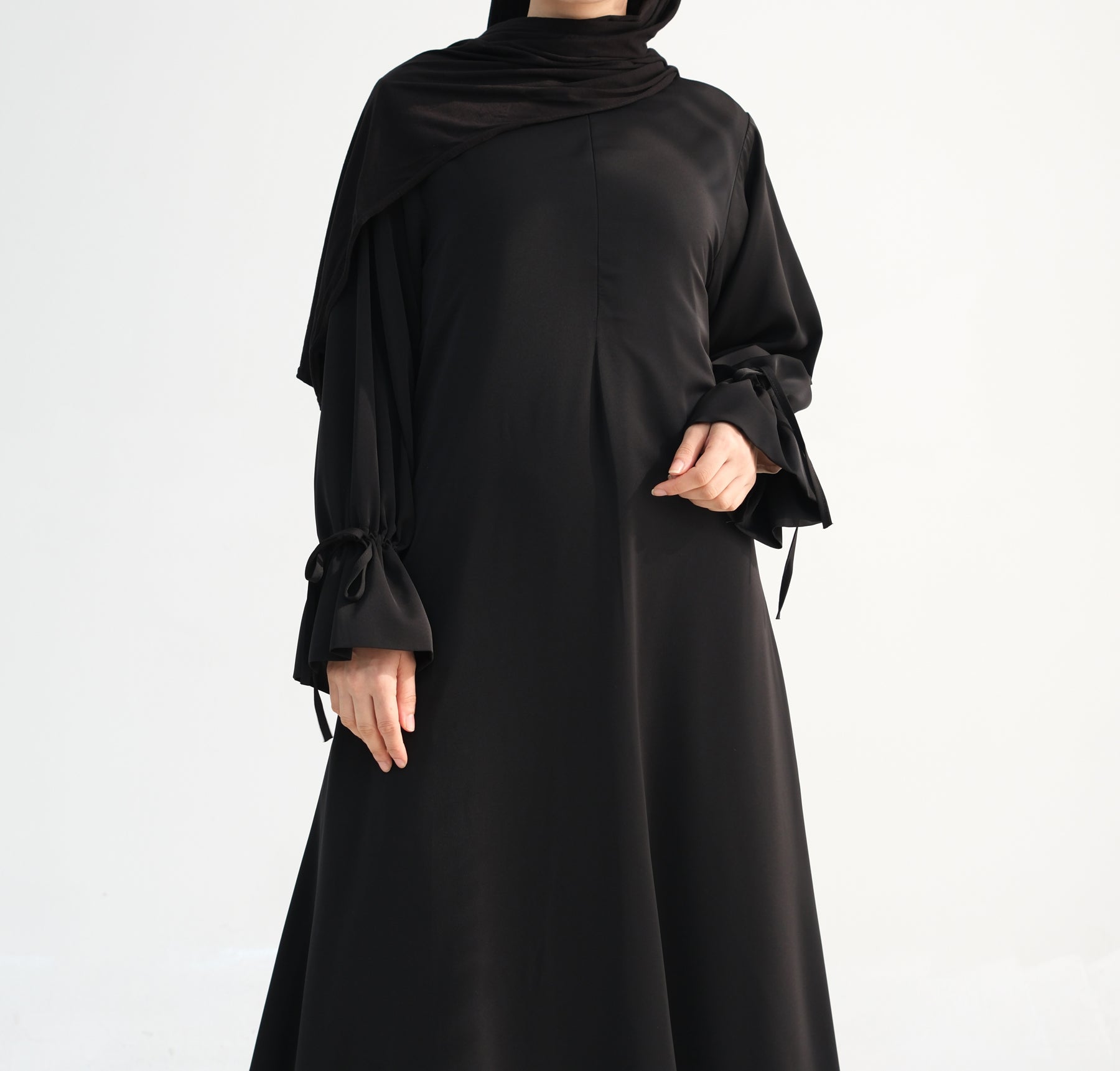 Black abaya worn by a model on a white background