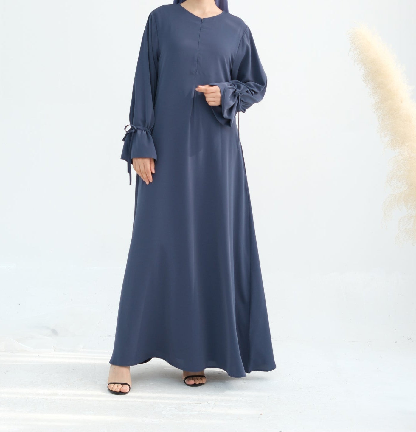 Woman wearing a long blue dress with bell sleeves on a white background