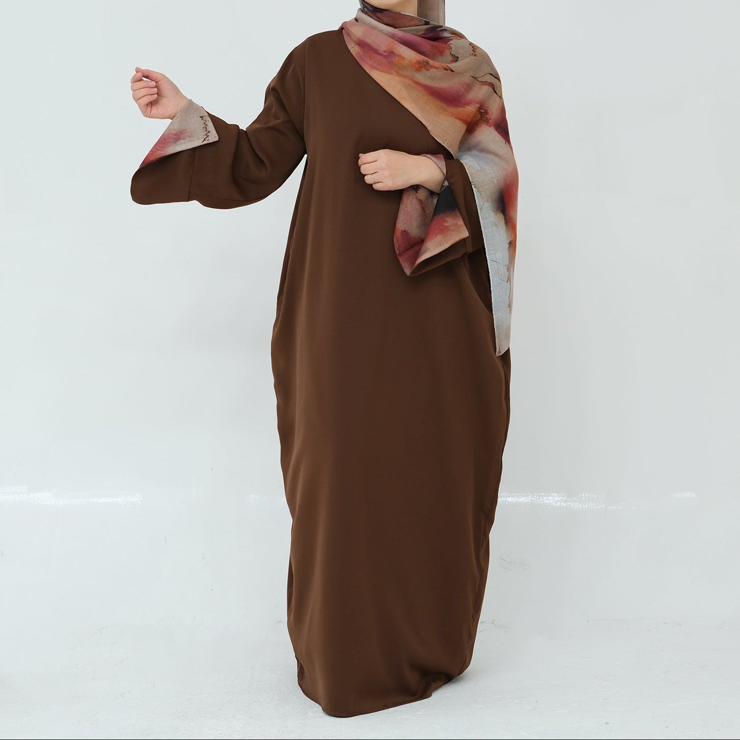 Woman wearing a brown dress with a patterned hijab on a white background