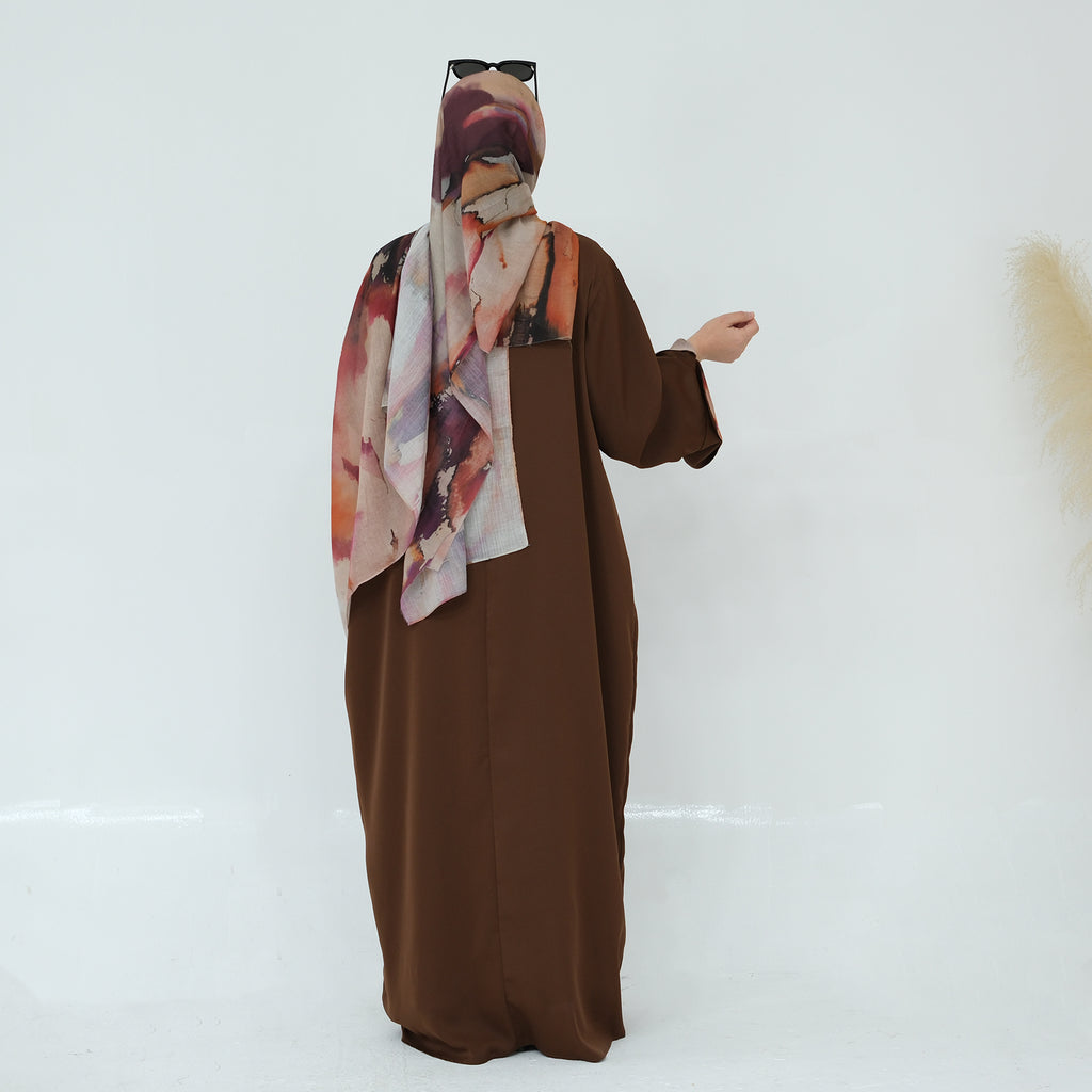 Person wearing a brown abaya with a patterned scarf on a white background