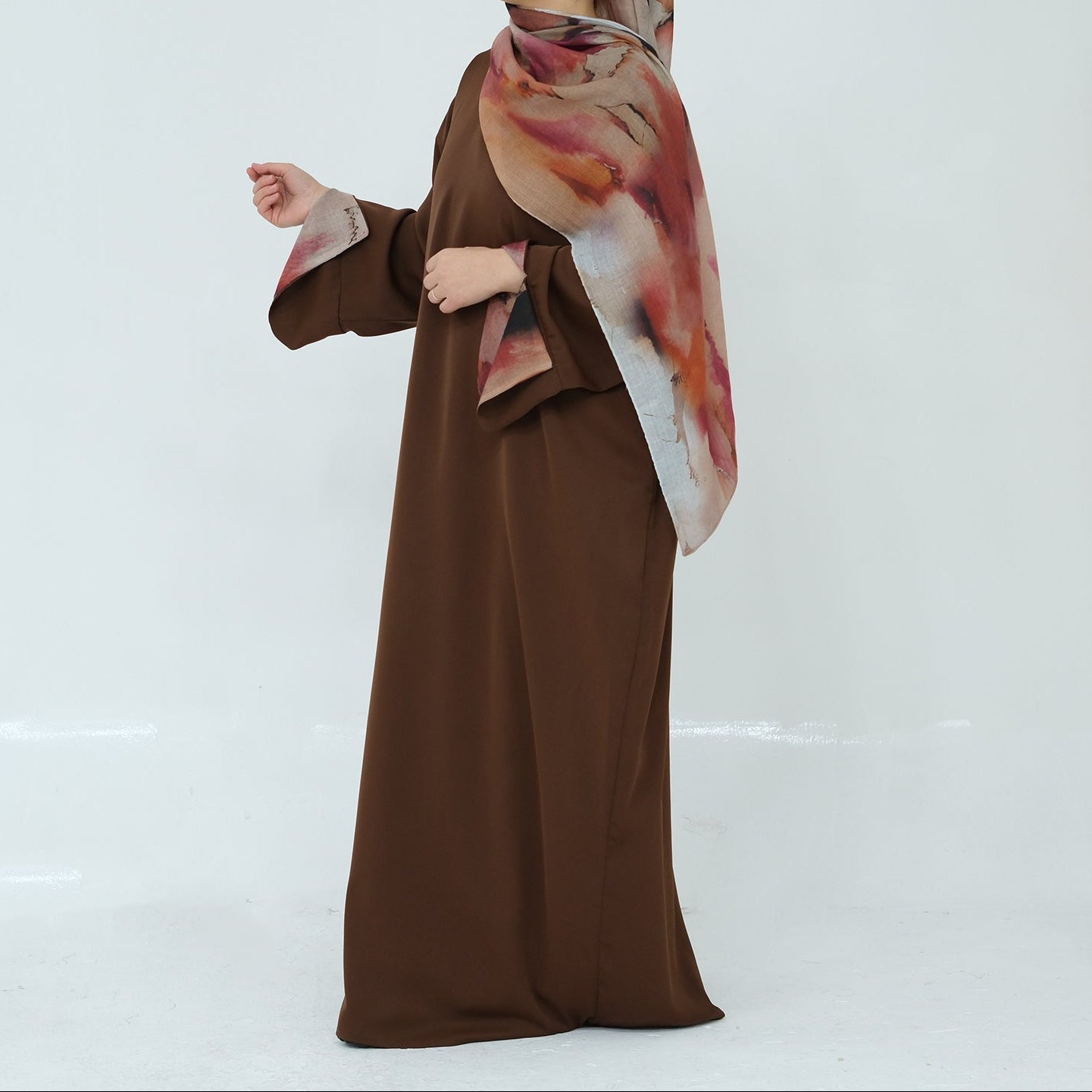 Woman wearing a brown abaya with a patterned hijab on a white background