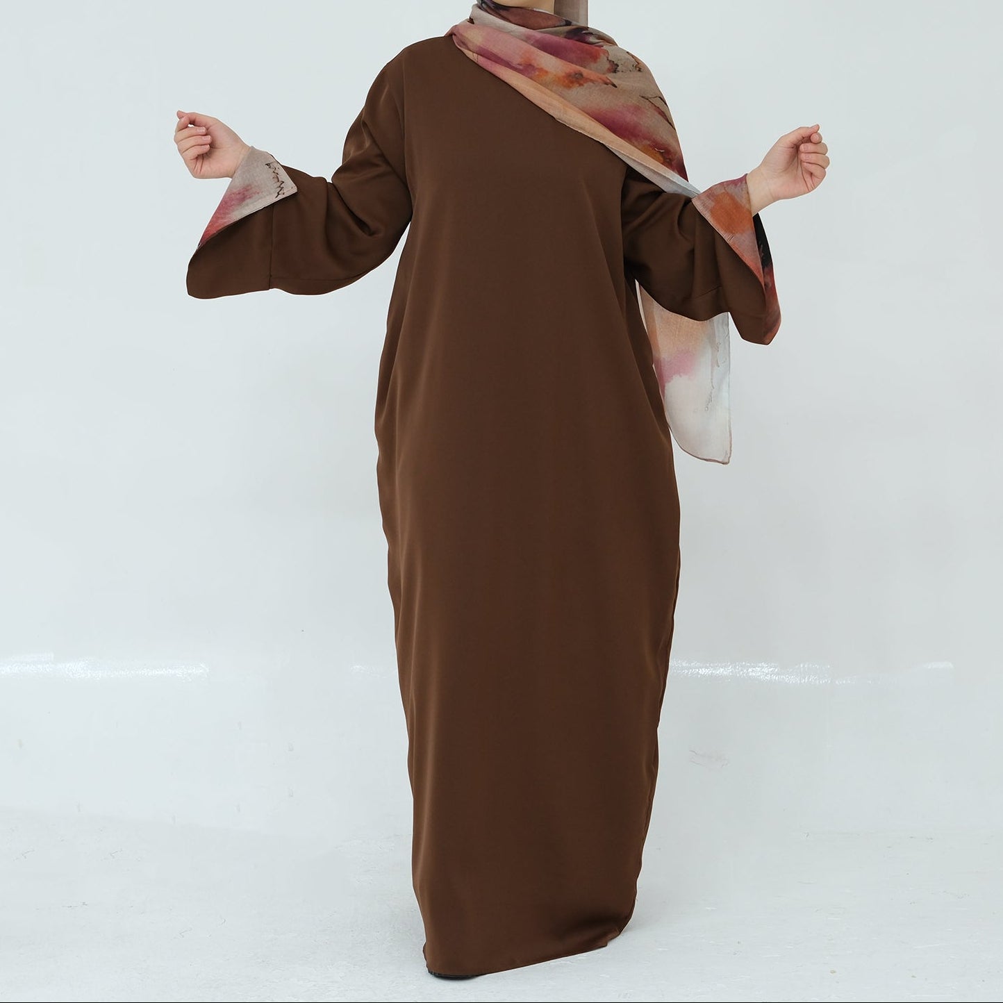 Woman wearing a brown dress with a patterned hijab on a white background