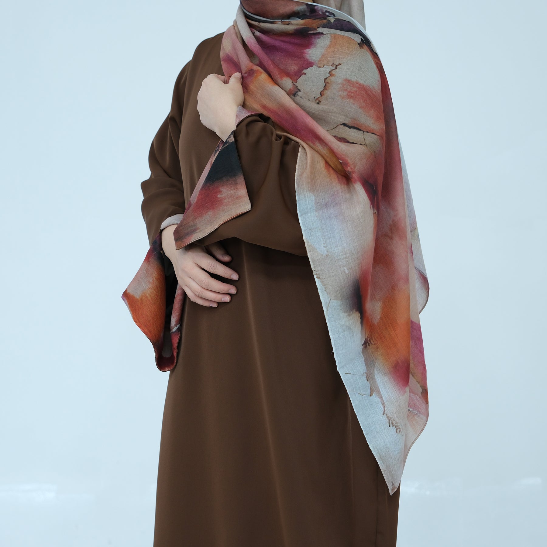 Person wearing a brown dress with a colorful scarf draped over the shoulder against a light blue background