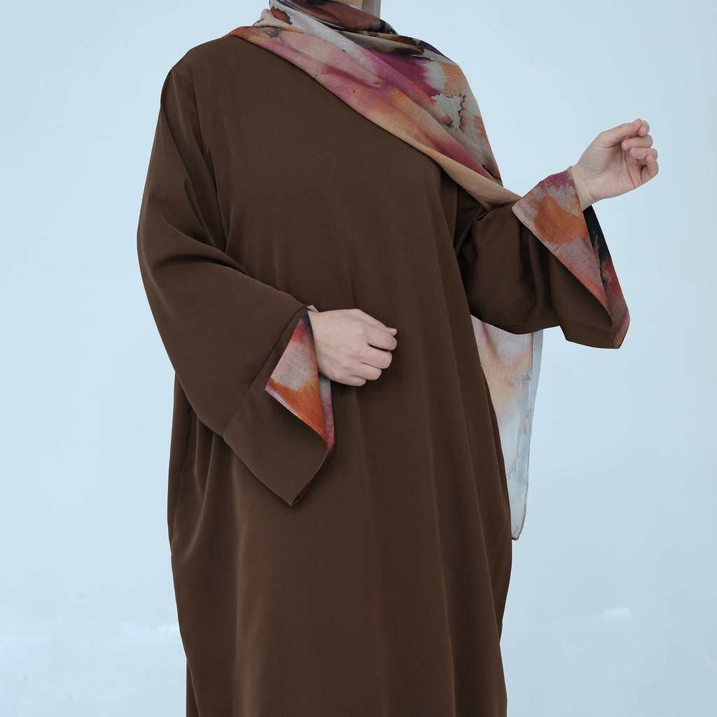 Person wearing a brown garment with a colorful scarf over shoulder on a light blue background