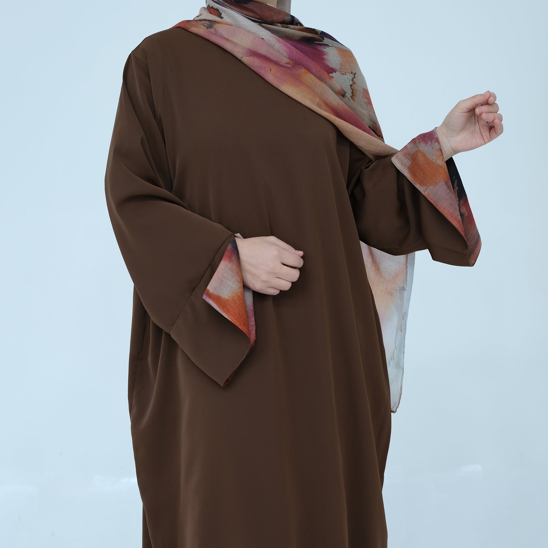 Person wearing a brown garment with a colorful scarf over shoulder on a light blue background