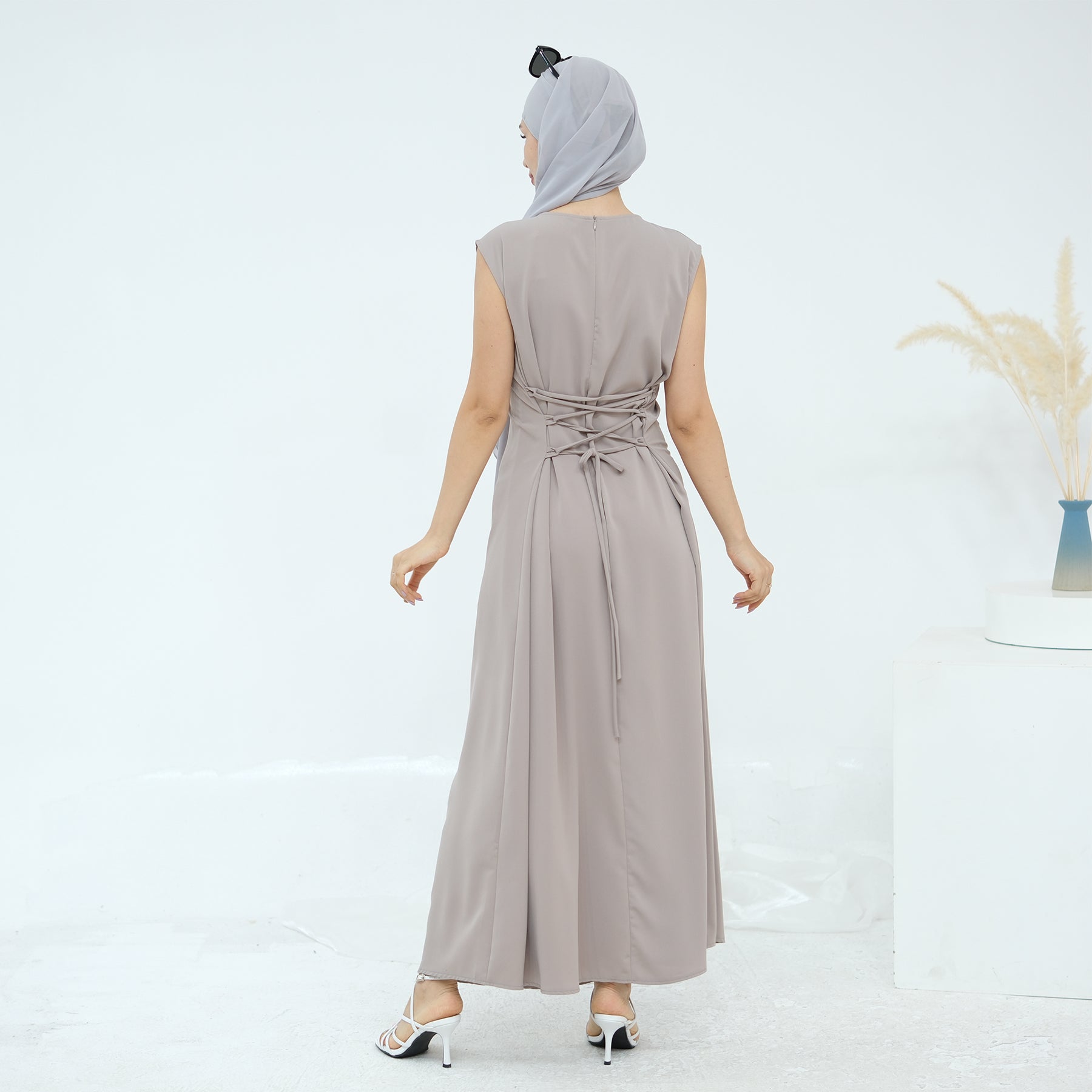 Woman wearing a long beige dress with a belt on a white background