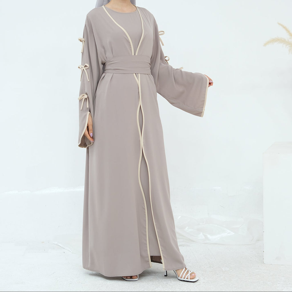 Woman wearing a gray abaya with white trim on a white background