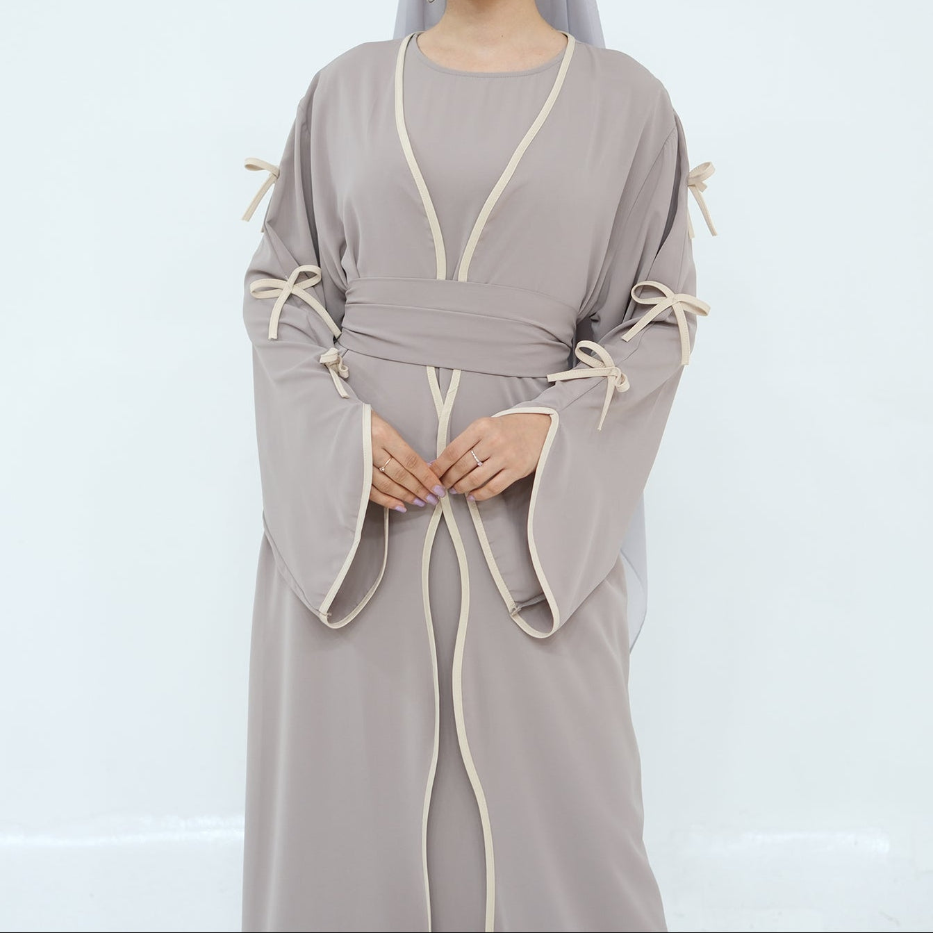 Woman wearing a gray abaya with white trim on a light gray background