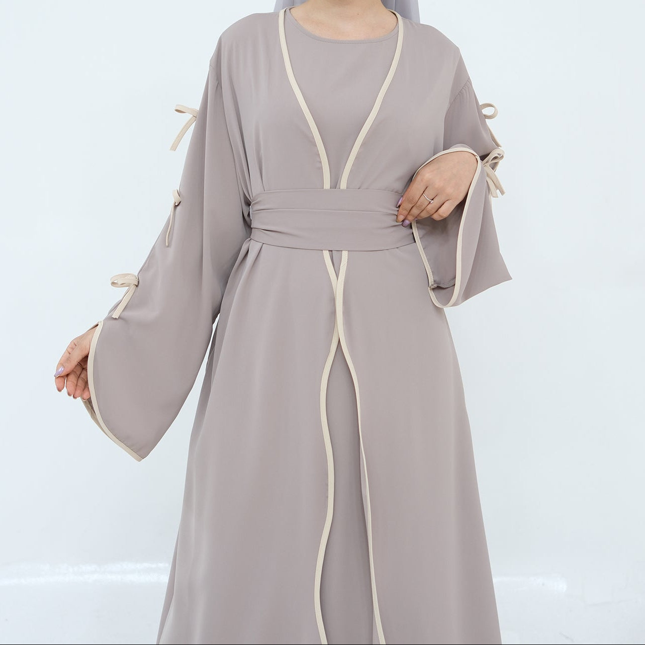 Woman wearing a long, light gray dress with a belt on a white background